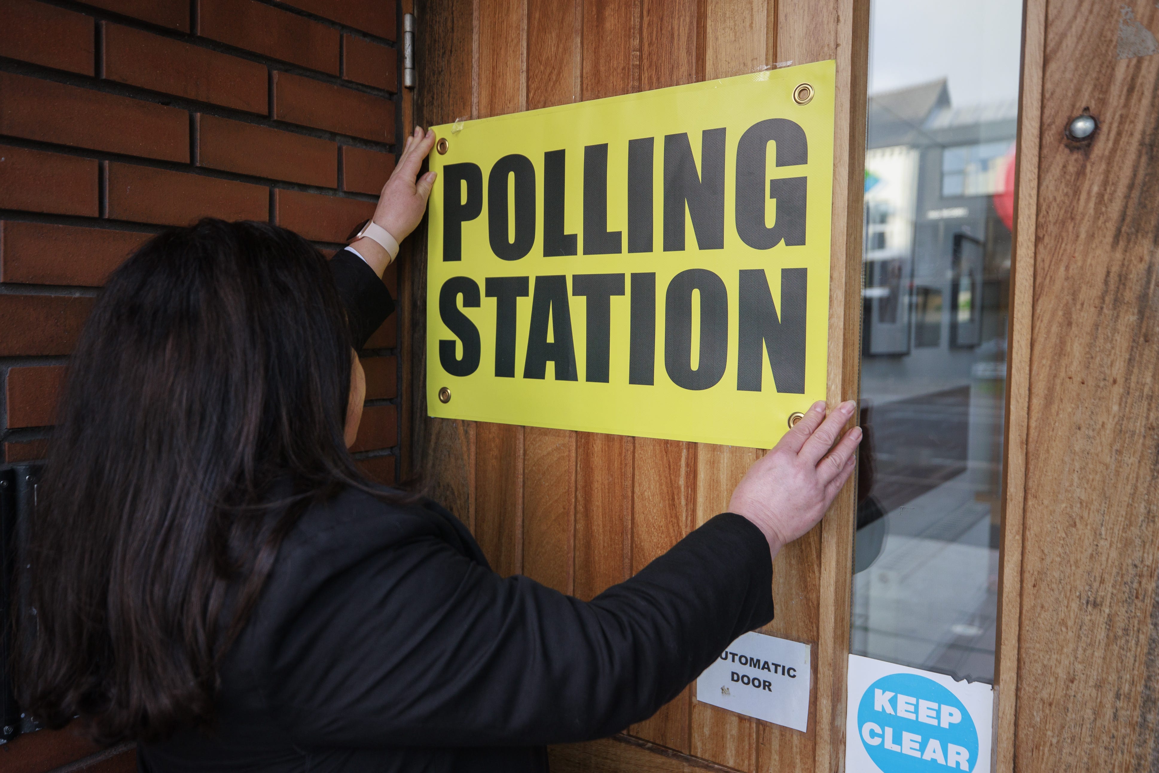 A member of the polling station team at the Agape Centre in south Belfast hangs a sign ahead of polling stations opening in the 2024 General Election (Liam McBurney/PA)