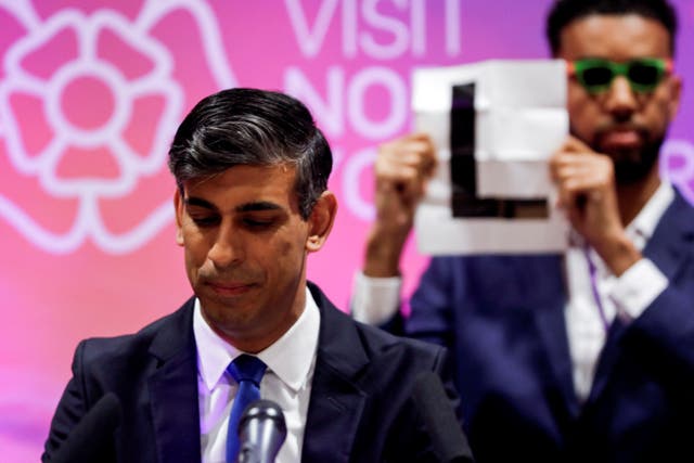 <p>Welcome to the losing side: a candidate holds up an ‘L’ sign behind Rishi Sunak, who has led the Conservatives to their worst election result in history </p>
