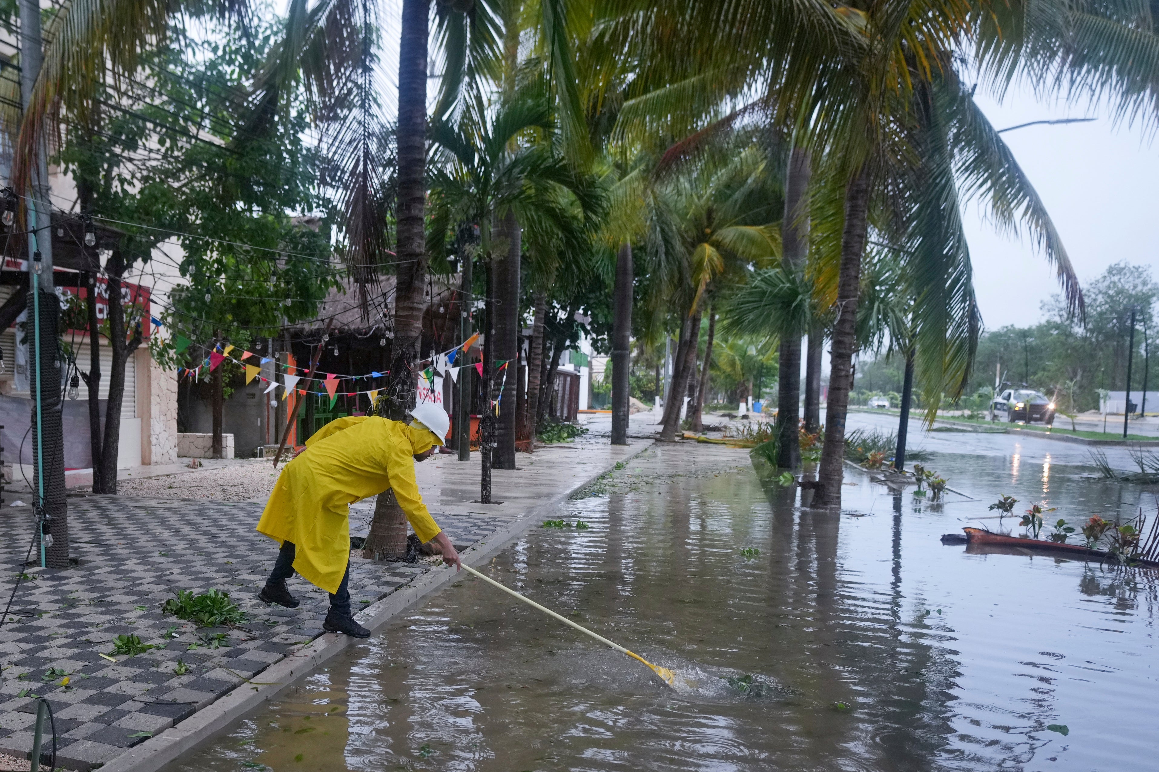 A man unclogs a drain in a flooded street after Beryl, now a tropical storm, hit Tulum Mexico on Friday
