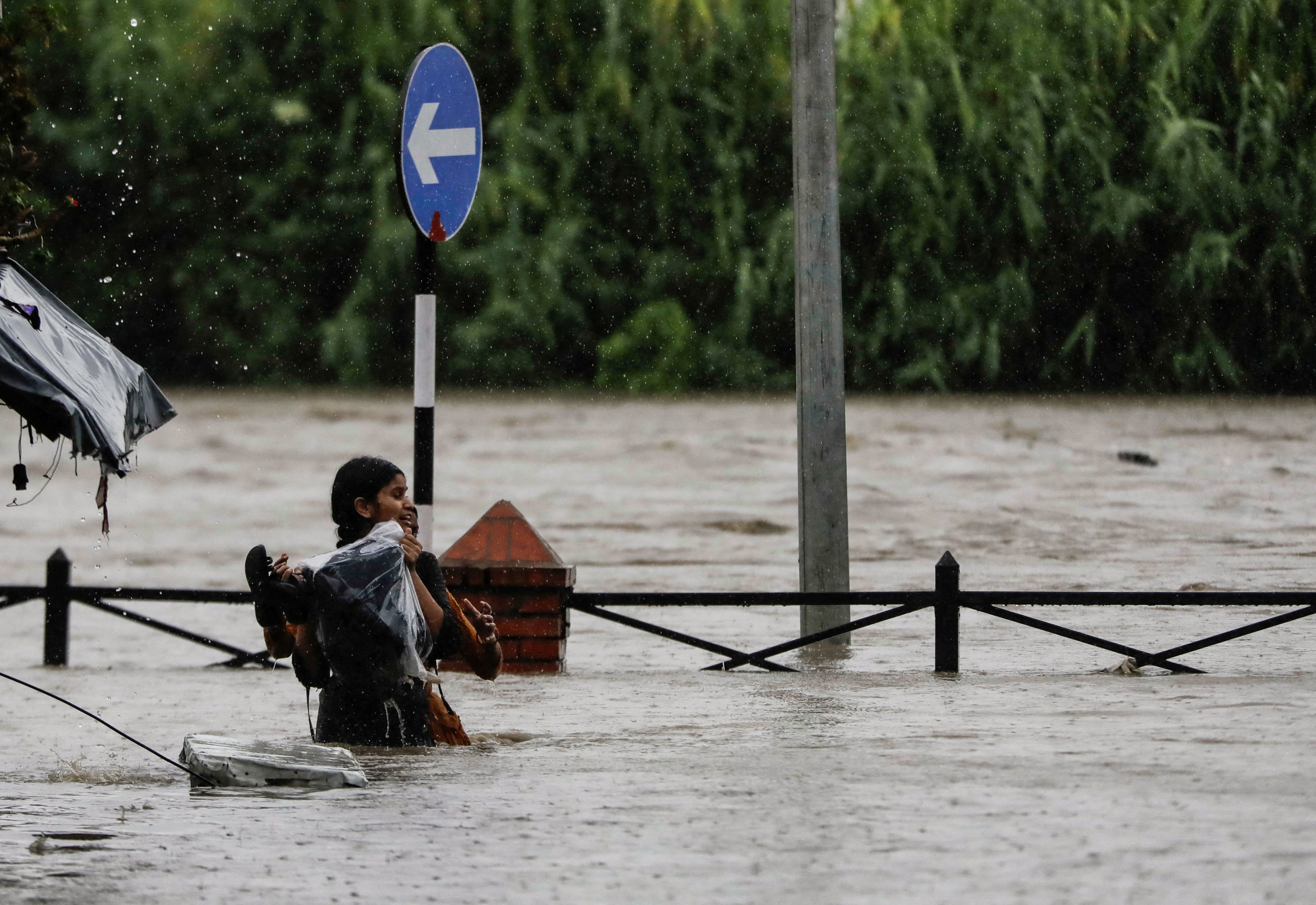 A woman carrying her belongings wades through a flooded road along the bank of the overflowing Bagmati river following heavy rains in Kathmandu, Nepal