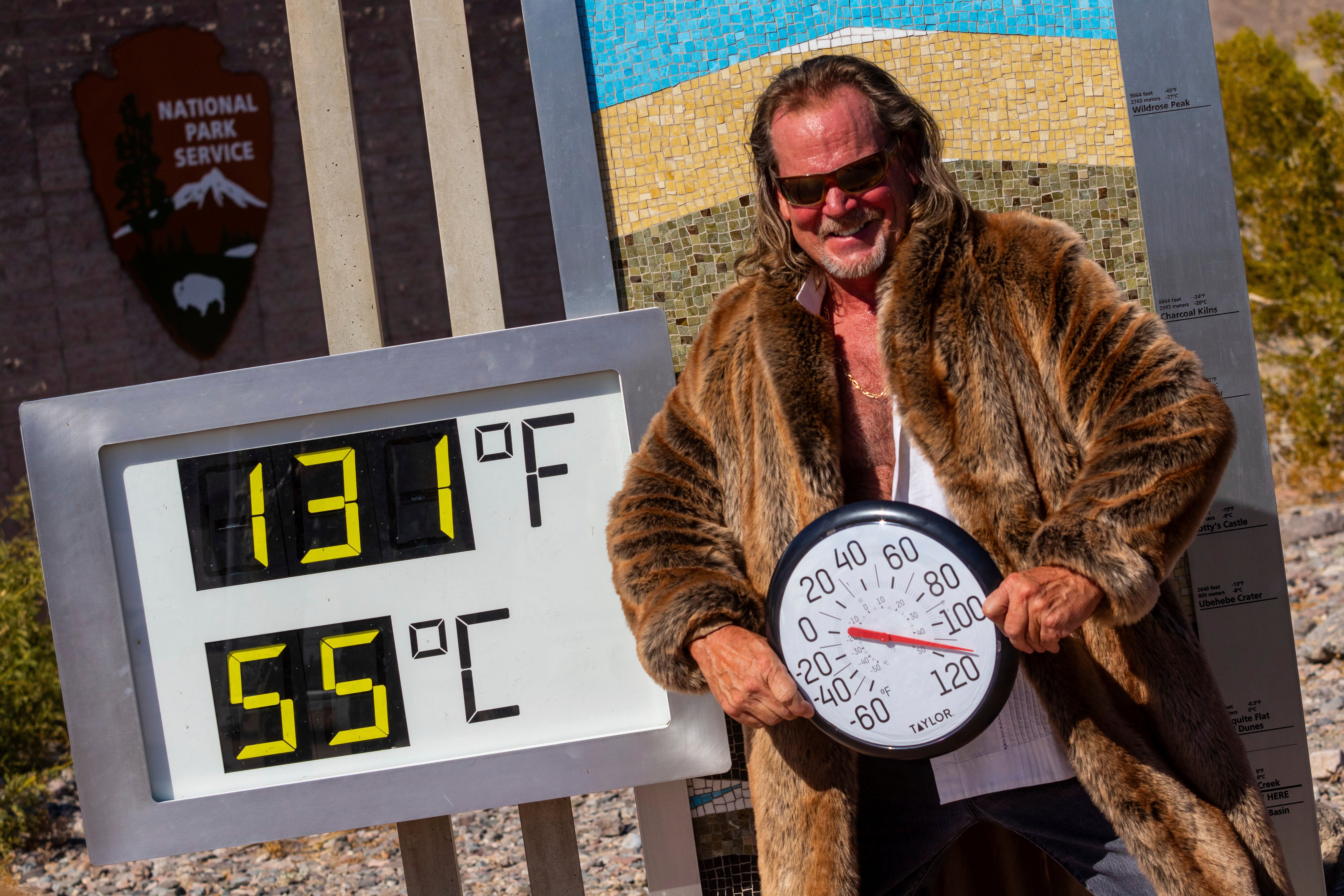 Thor Teigen poses in a fur jacket next to a thermometer displaying a temperature of 131 degrees Fahrenheit / 55 degrees Celsius at the Furnace Creek Visitors Center, in Death Valley National Park