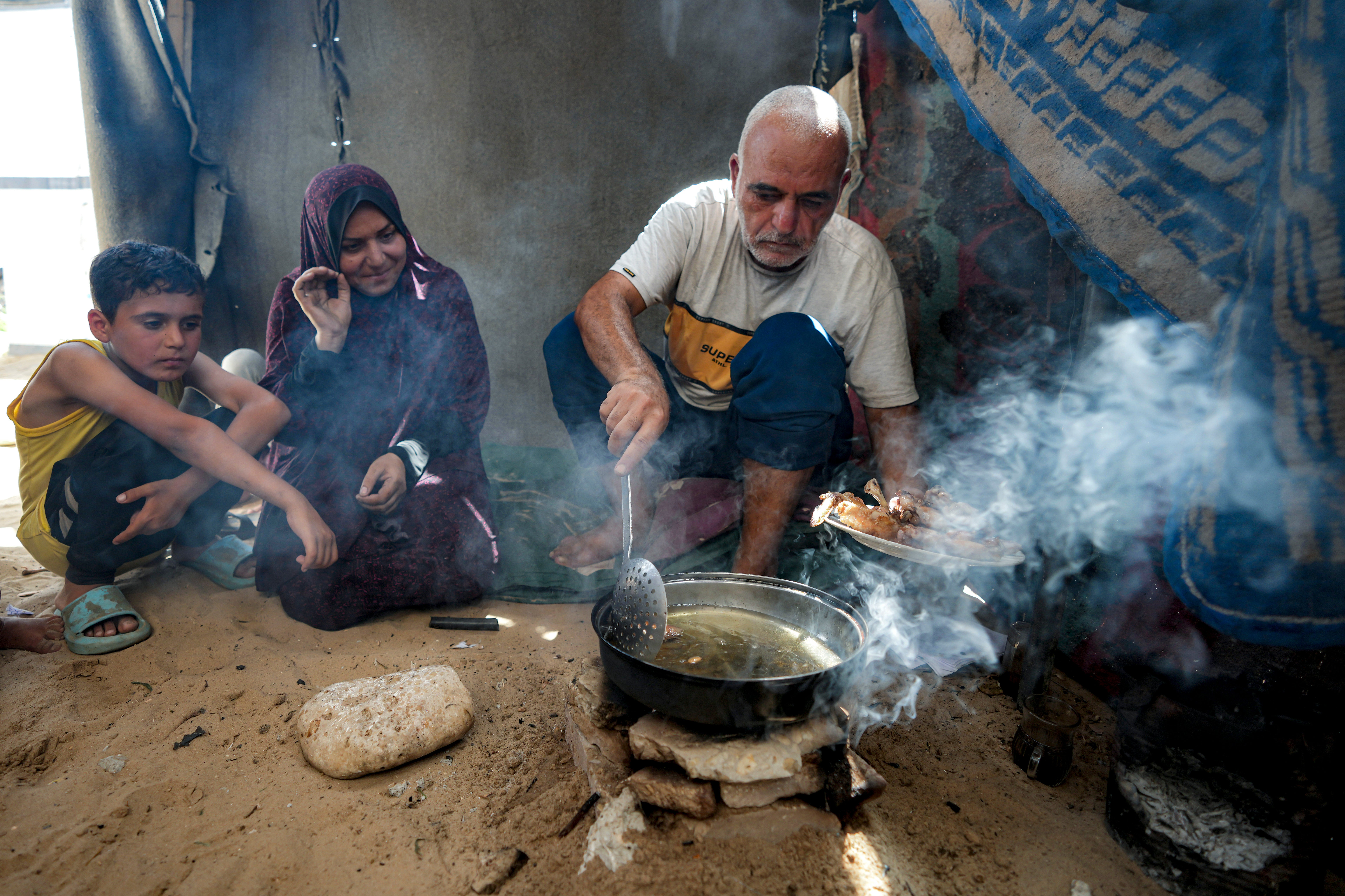 Hassan Nofal, right, who was displaced by the Israeli bombardment of the Gaza Strip, prepares lunch with his family at a makeshift tent camp in Khan Younis