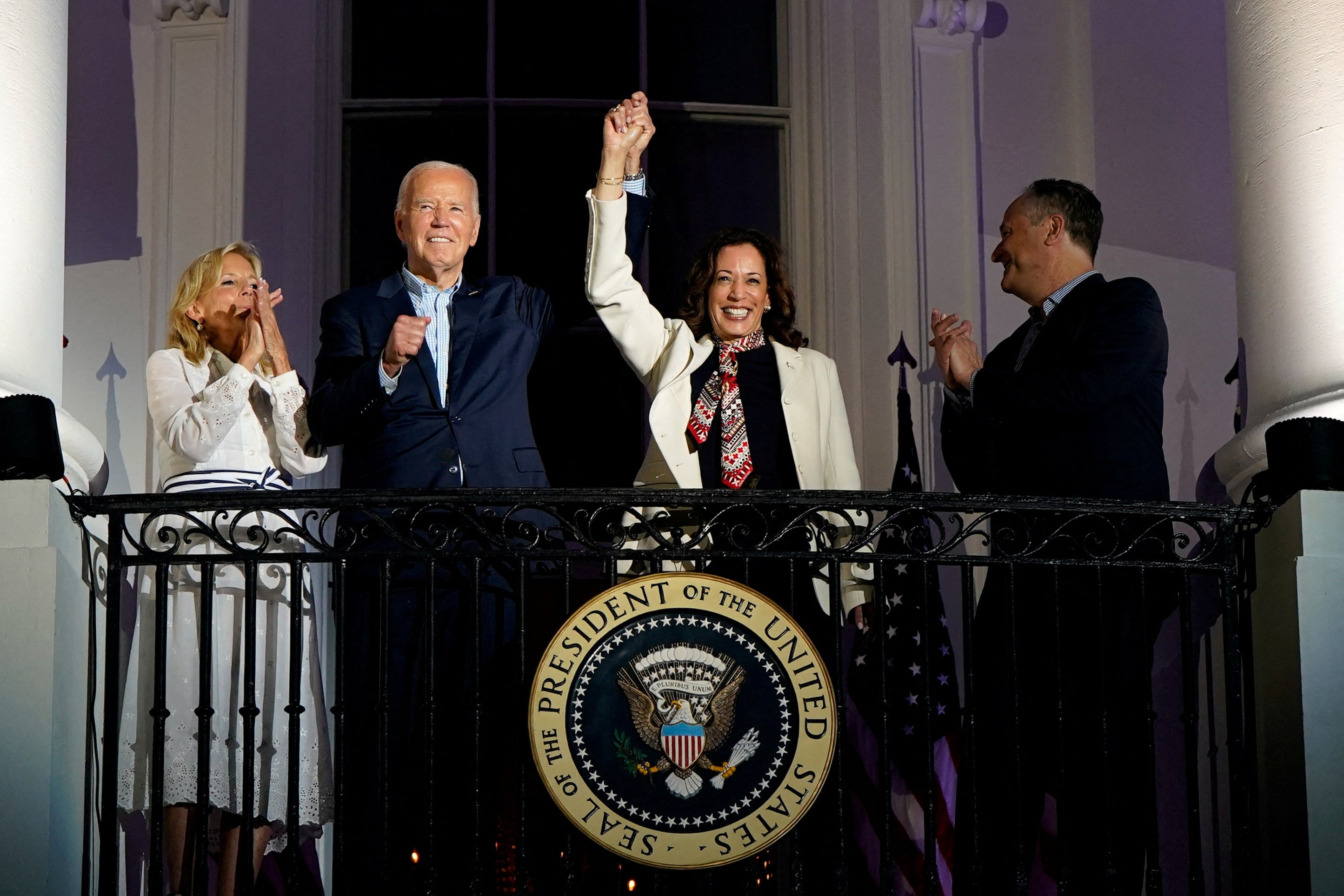 President Joe Biden and Vice President Kamala Harris raise their hands as they stand on a White House balcony with first lady Jill Biden and second gentleman Doug Emhoff during an Independence Day celebration