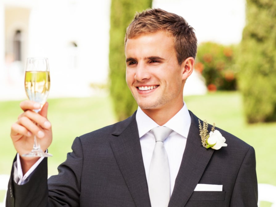 Happy young best man looking away while toasting champagne flute at garden wedding ( Getty Images )
