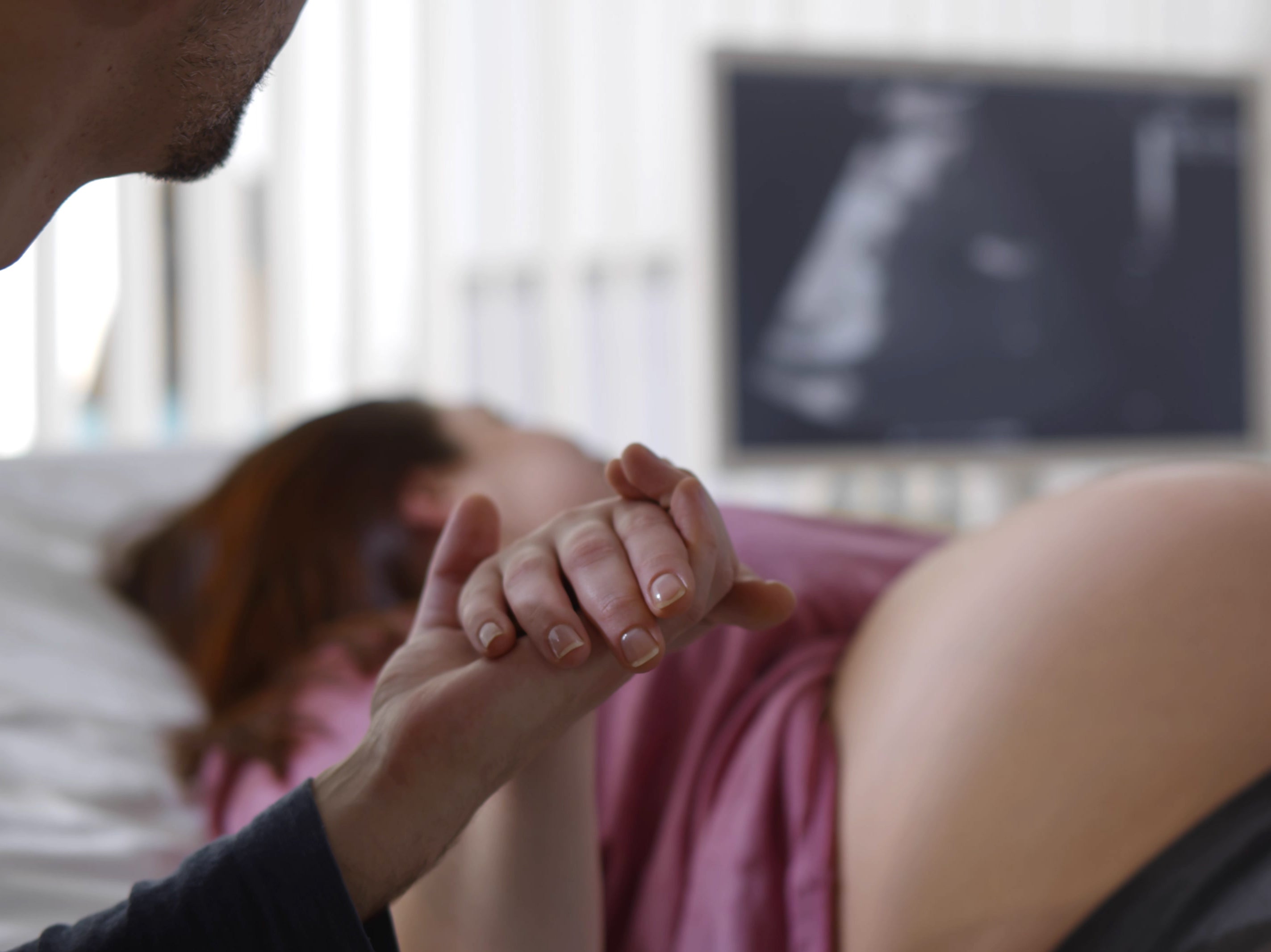 Close-up of a man holding his pregnant wife's hand during an ultrasound scan at a clinic (Getty Images)