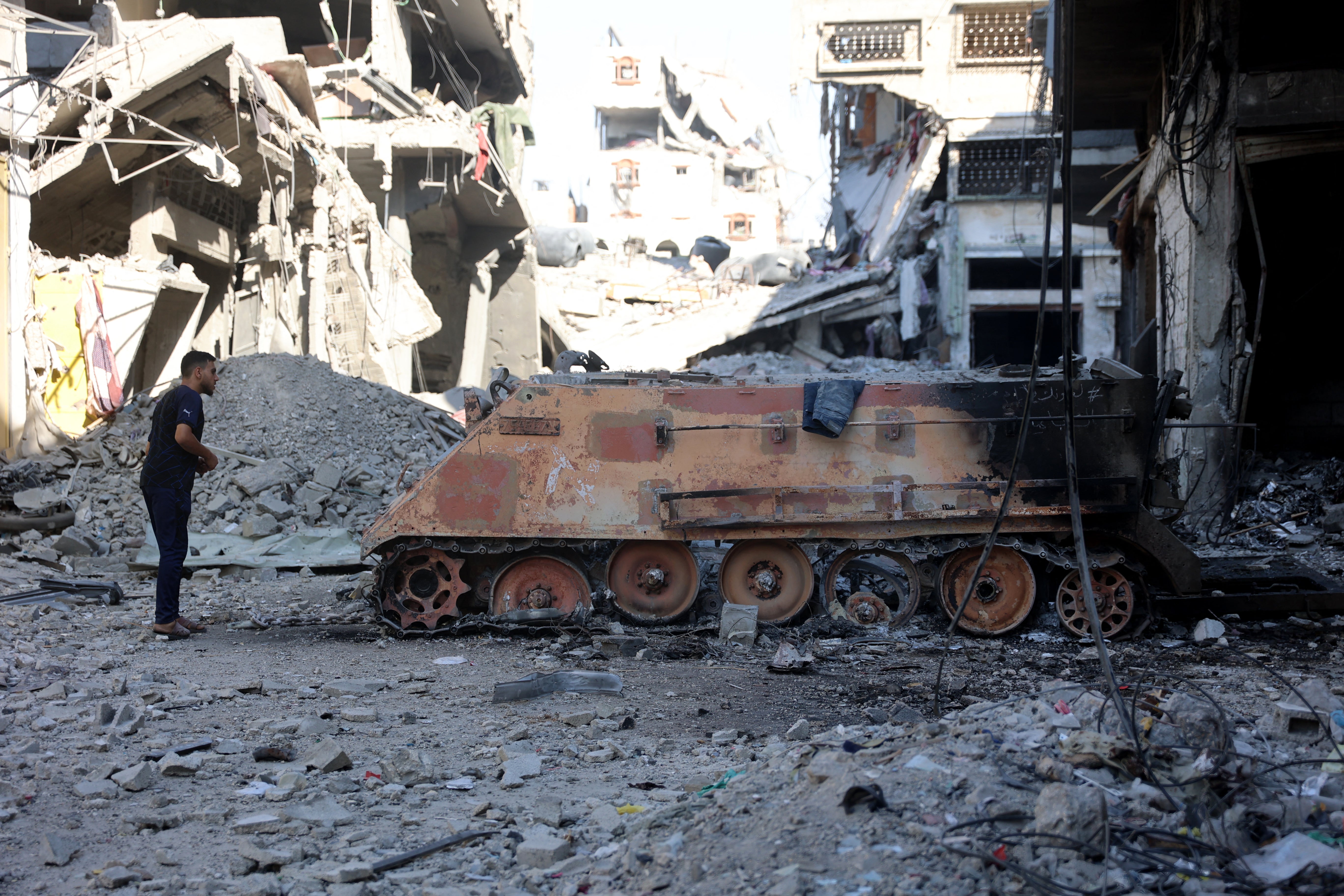 A Palestinian man looks at a destroyed Israeli military vehicle seen near the destroyed buildings and rubble