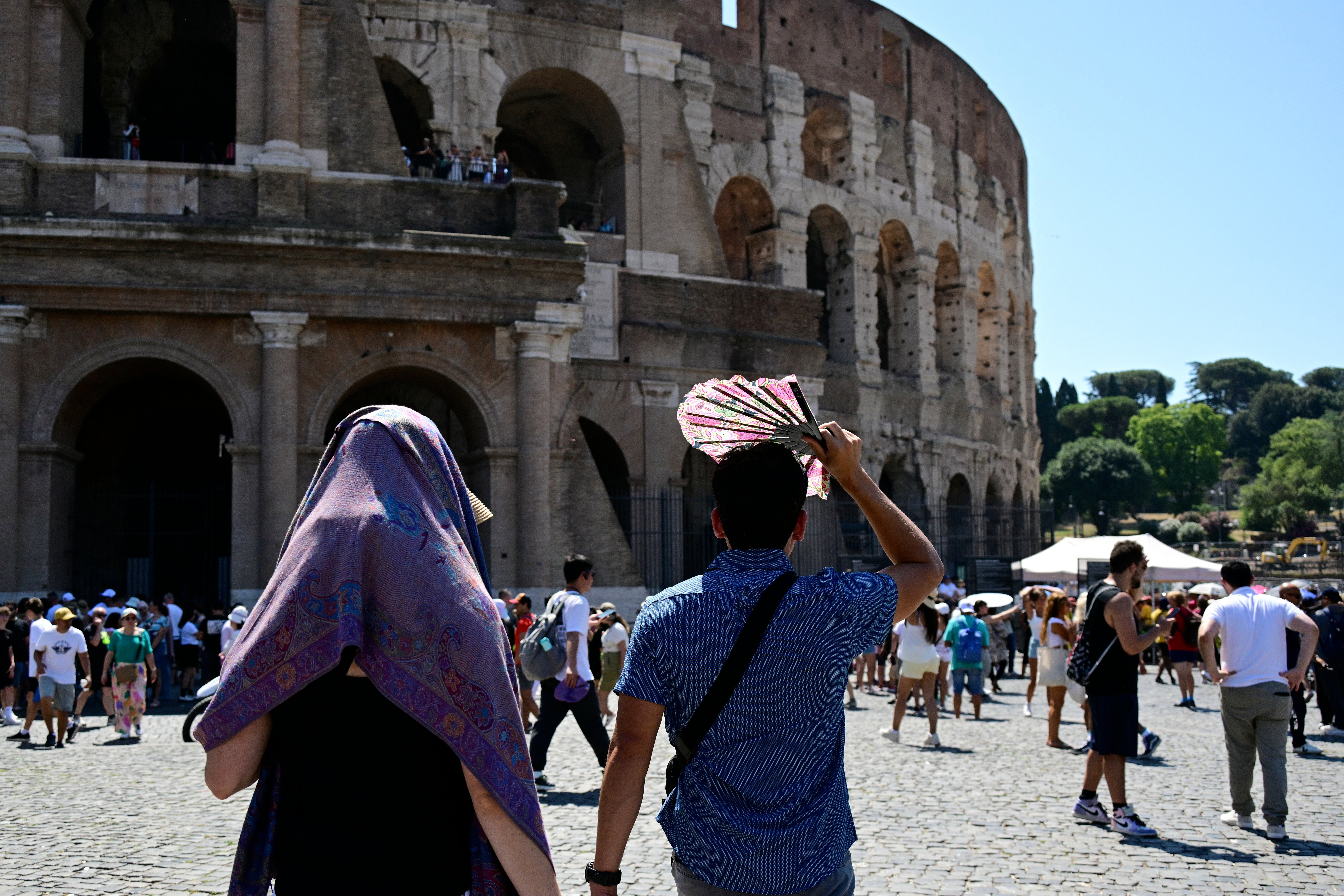 Tourists protect themselves from the sun as they walk near the Colosseum on July 11, 2024 in Rome where temperatures reach 38 degrees celsius