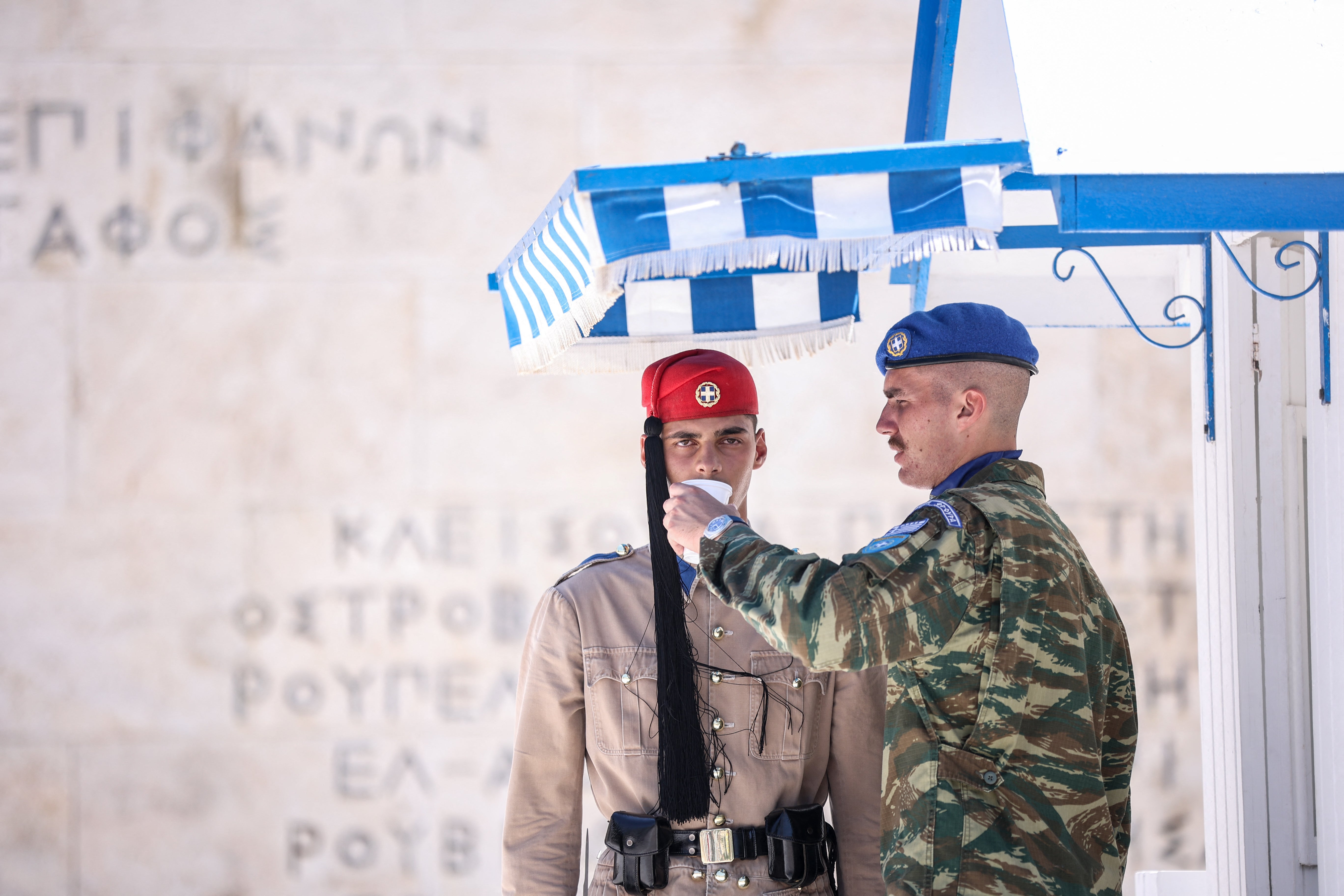 A police officer gives water to a member of the presidential guard in front of the Monument to the Unknown Soldier at Syntagma Square in Athens on July 12, 2024.