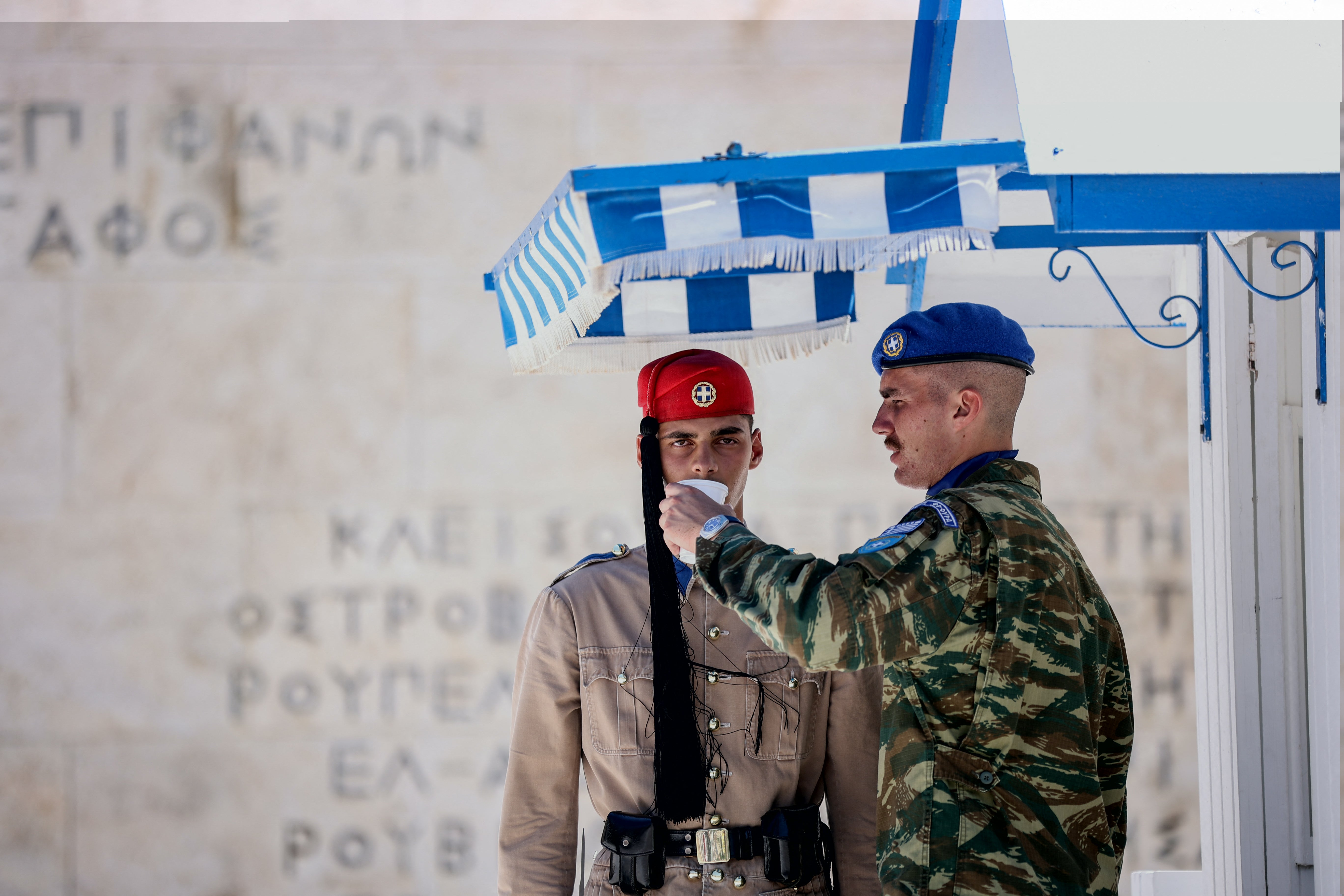 Um oficial dá água a um membro da guarda presidencial em frente ao monumento do Soldado Desconhecido na Praça Syntagma, em Atenas, em 12 de julho de 2024