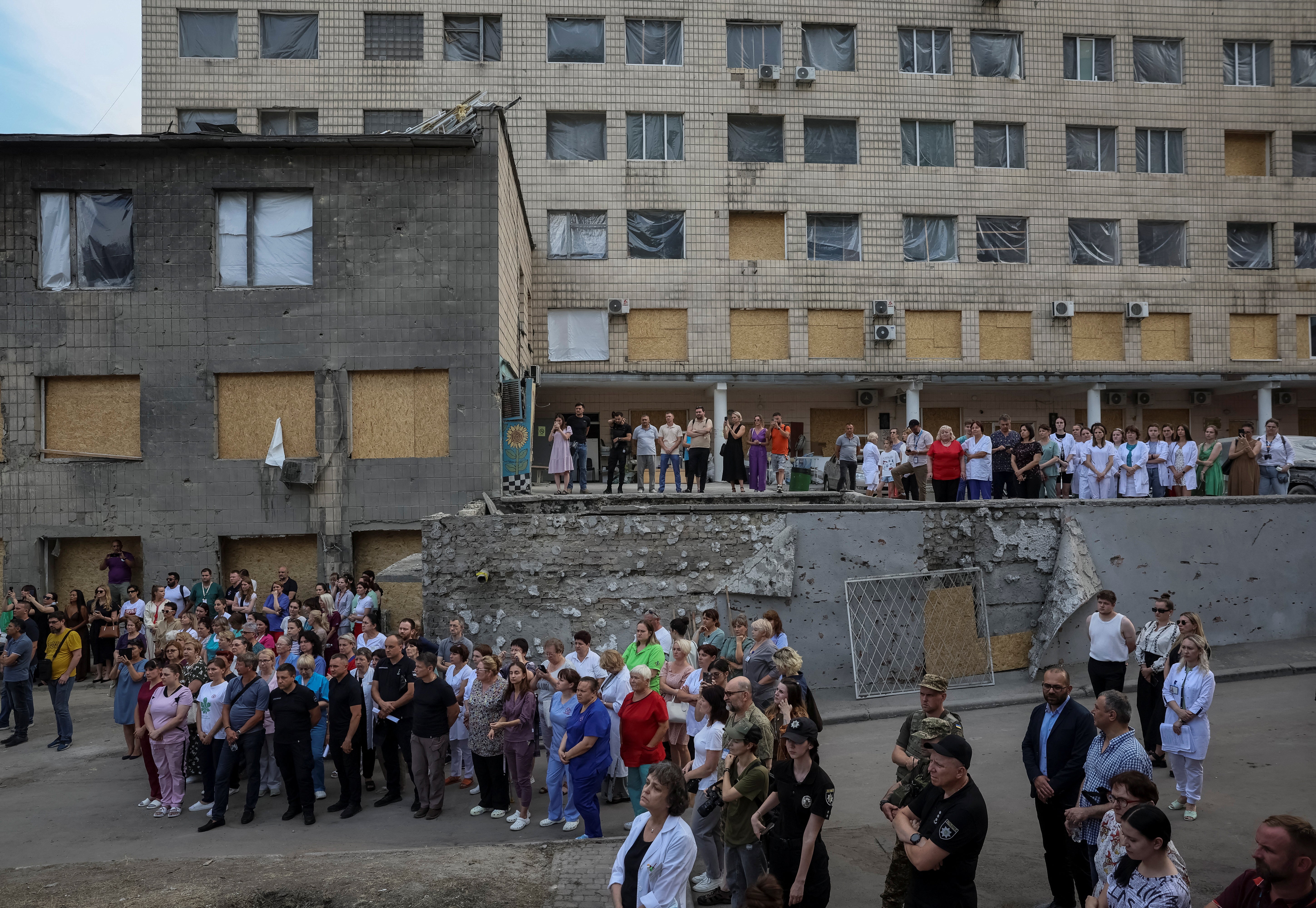 Dozens of medical workers watch the performance from the ruins of Okhmatdyt Children’s Hospital