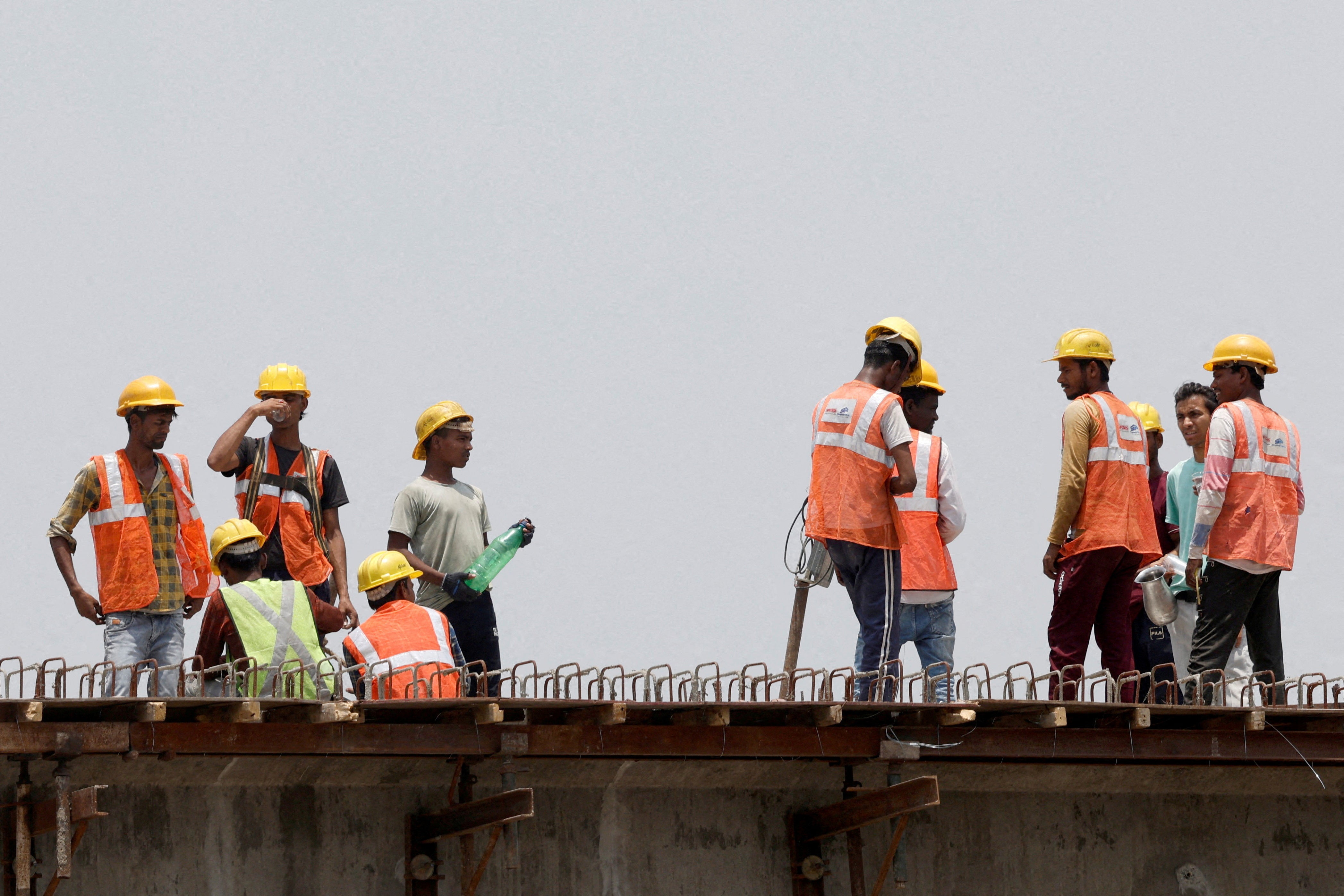 Indian workers drink water as they take a break at a construction site on a hot summer day