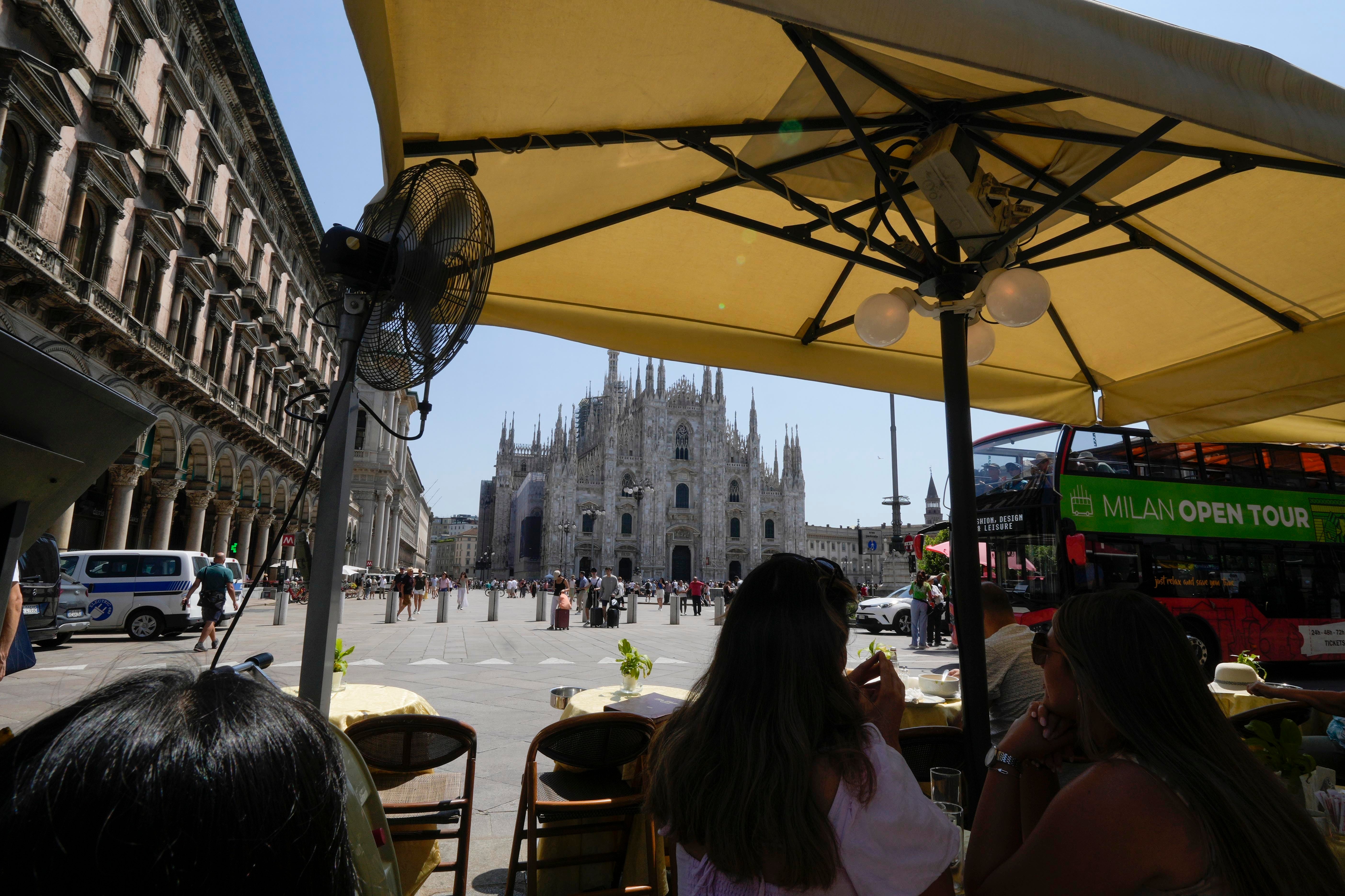 Tourists eat under an umbrella at a restaurant in front of the Duomo gothic cathedral, in Milan, Italy, Tuesday, July 16, 2024