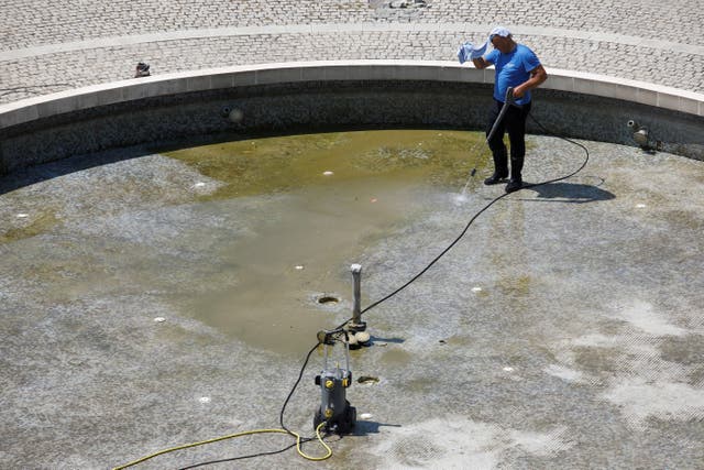 <p>A worker put a wet towel on his head to protect himself from the heat while cleaning a fountain in downtown Podgorica, Montenegro</p>