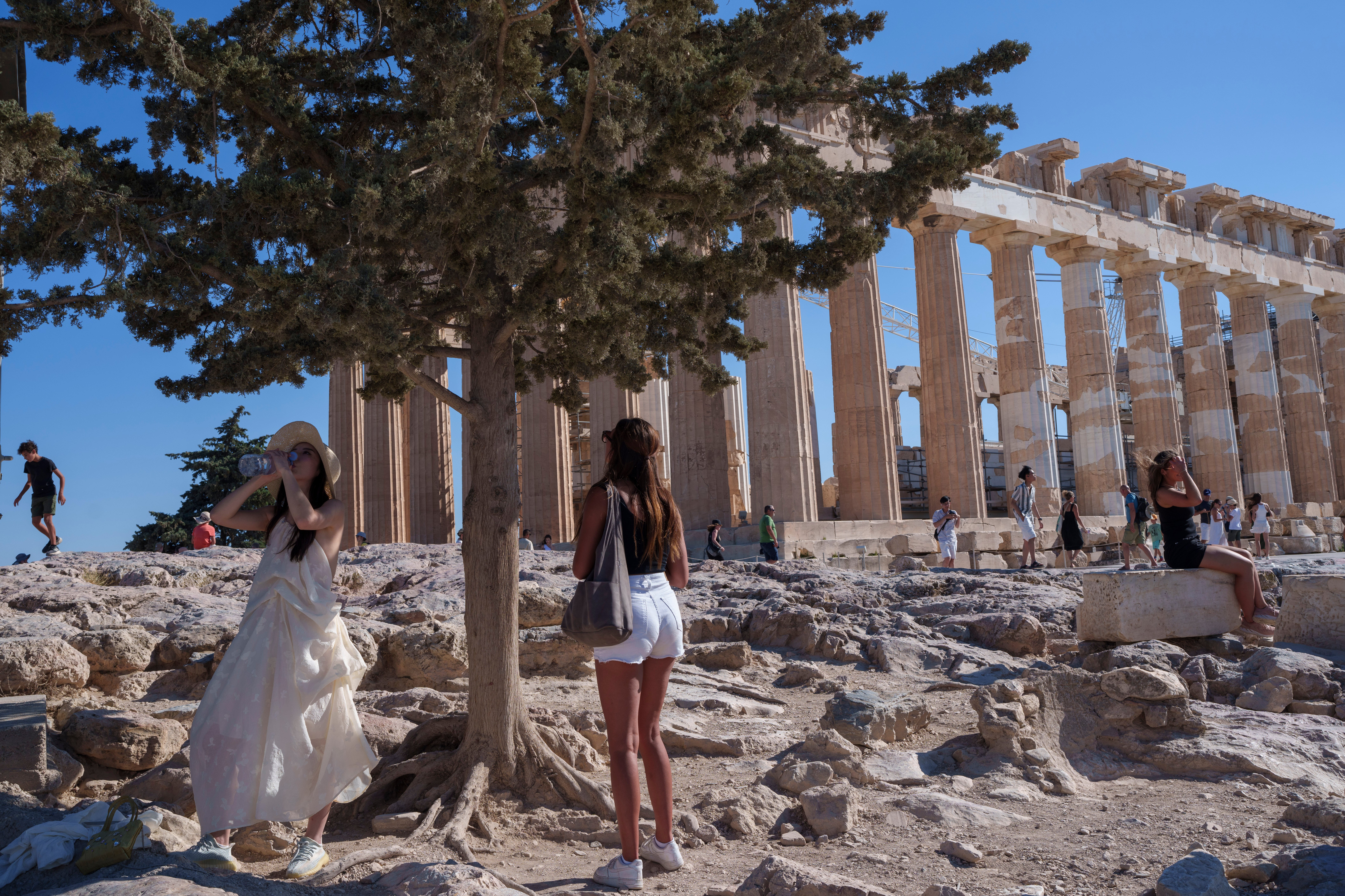 A woman drinks water in front of the ancient Parthenon Temple during a hot, windy day at Acropolis hill , in Athens, Tuesday, July 16, 2024