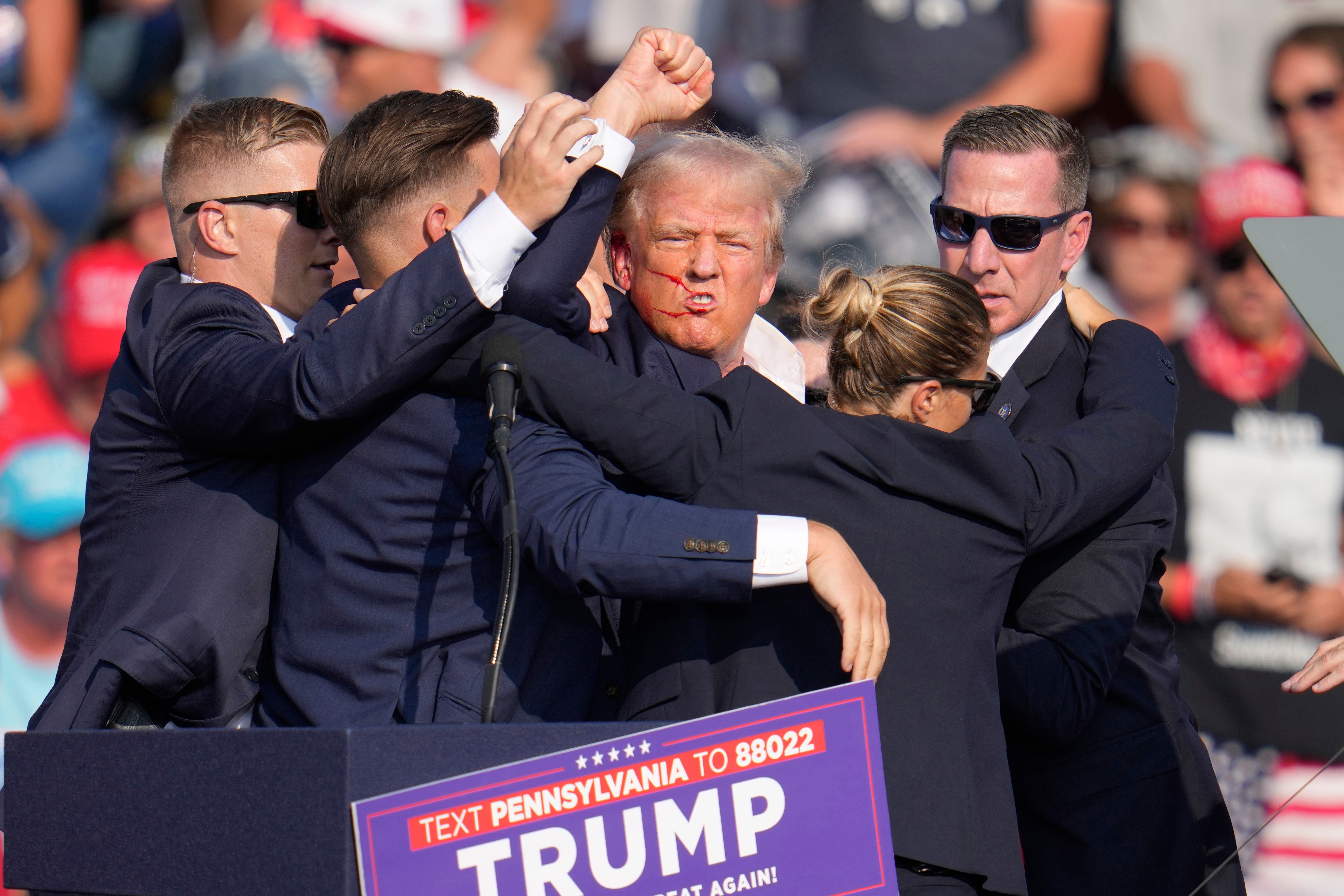 An injured Donald Trump surrounded by agents on stage following the assassination attempt