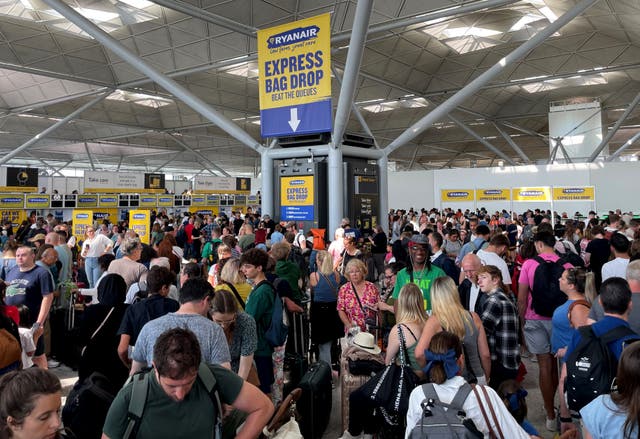 <p>Passengers queue by the Ryanair check-in desk at London Stansted Airport in Essex</p>