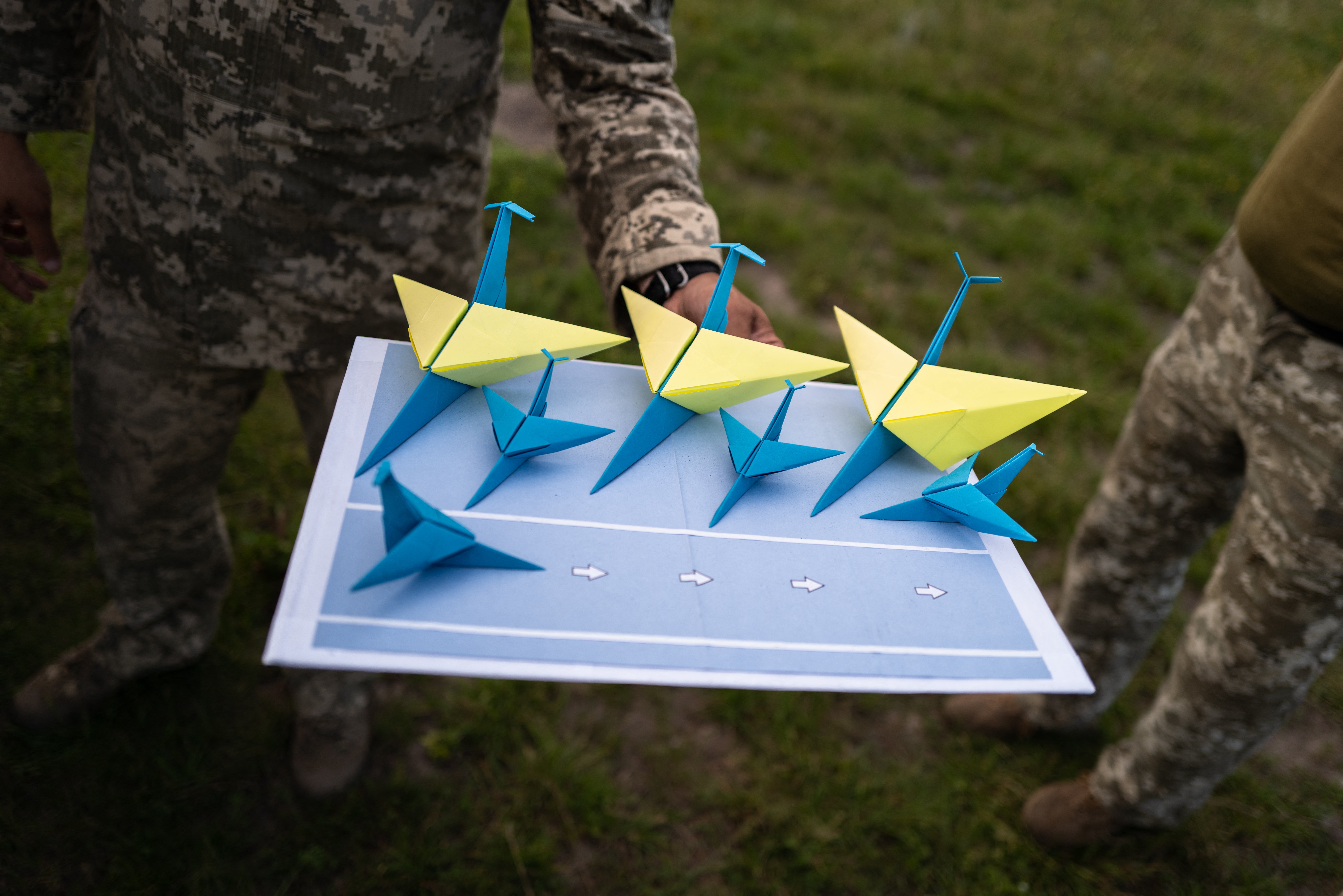A soldier from the Mobile Air Defense Brigade holds an origami model of an air force base near a training ground in the Khmelnitsky region