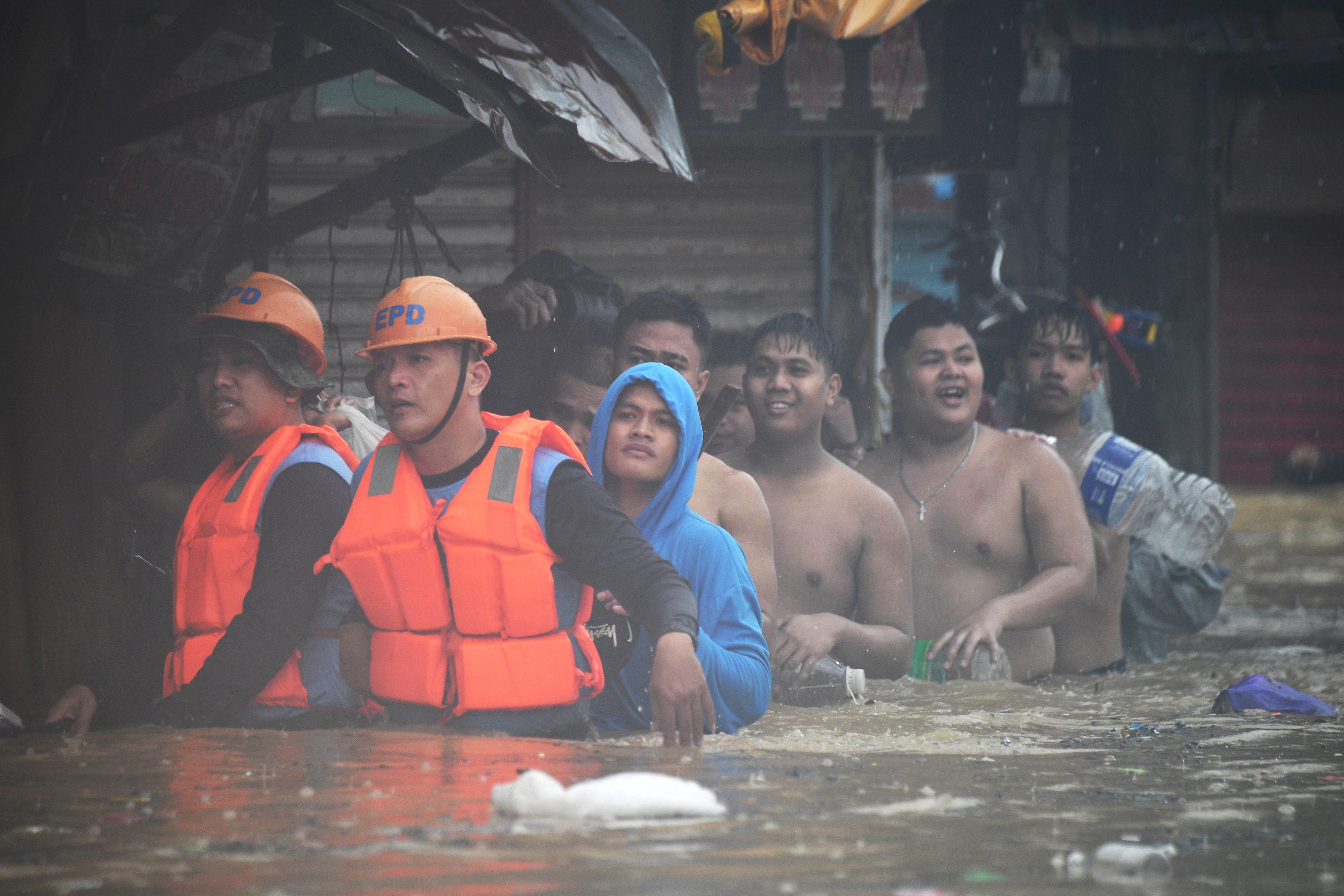 Reddingswerkers (van voren naar links) begeleiden bewoners met hun bezittingen terwijl ze worden geëvacueerd uit hun ondergelopen huizen in Tumana Village, Marikina City, ten oosten van Manilla.