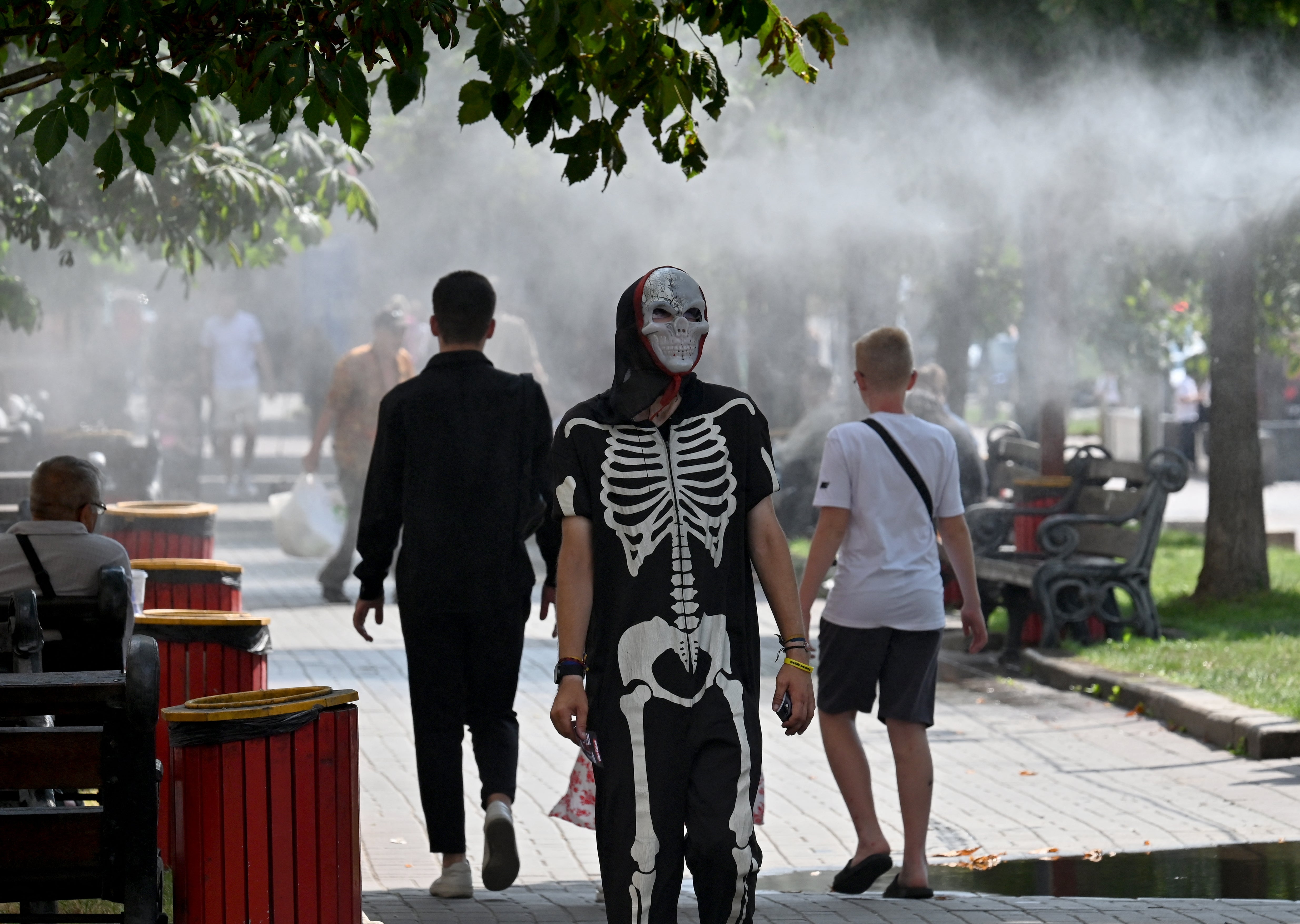 A man wearing a skeleton costume (C) hands out advertising flyers to passersby walking along water misters to cool down in the centre of Kyiv during a heatwave