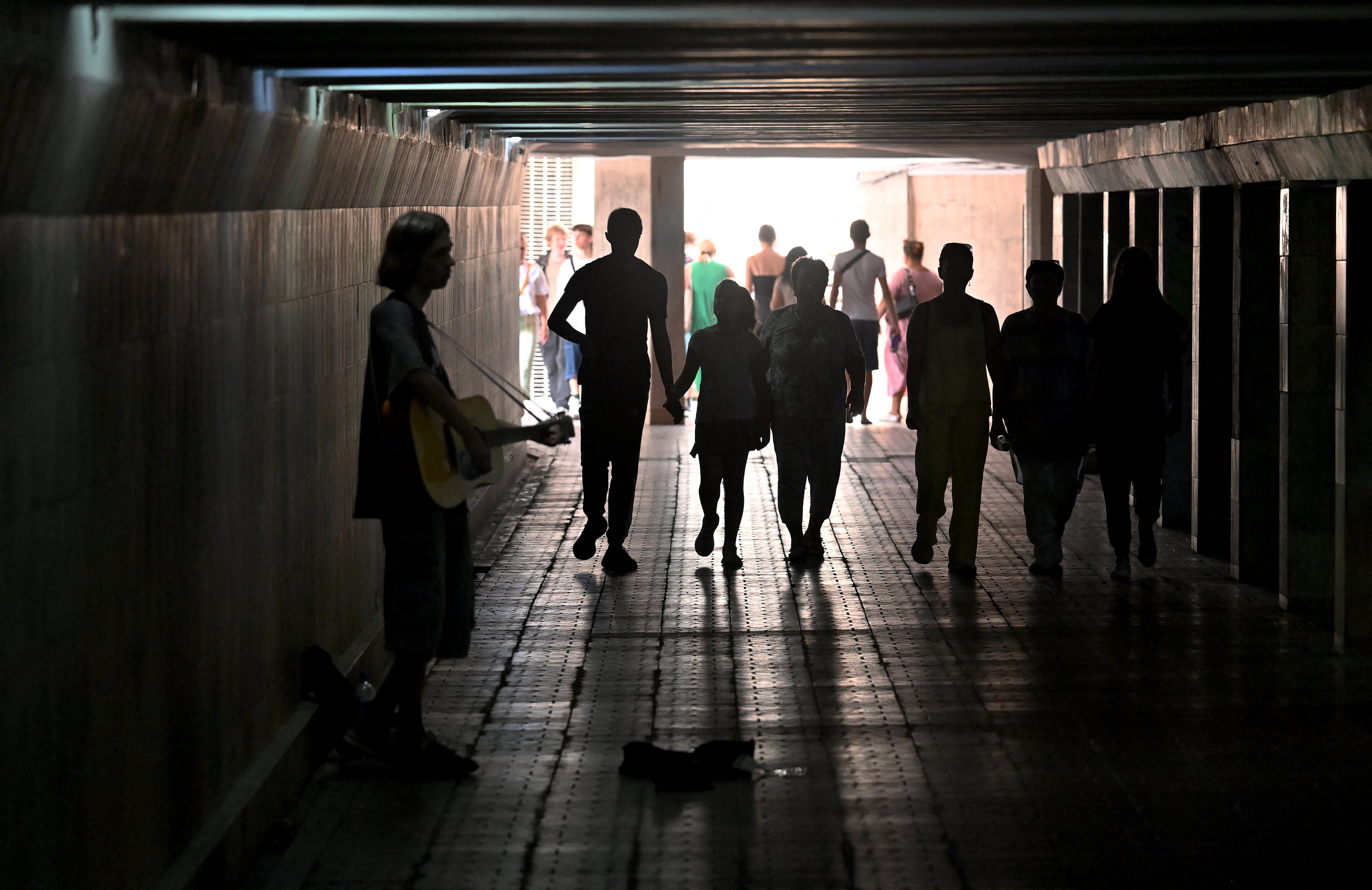 Pedestrians walk past a guitarist playing in an underground pedestrian way in the centre of Kyiv during a heatwave