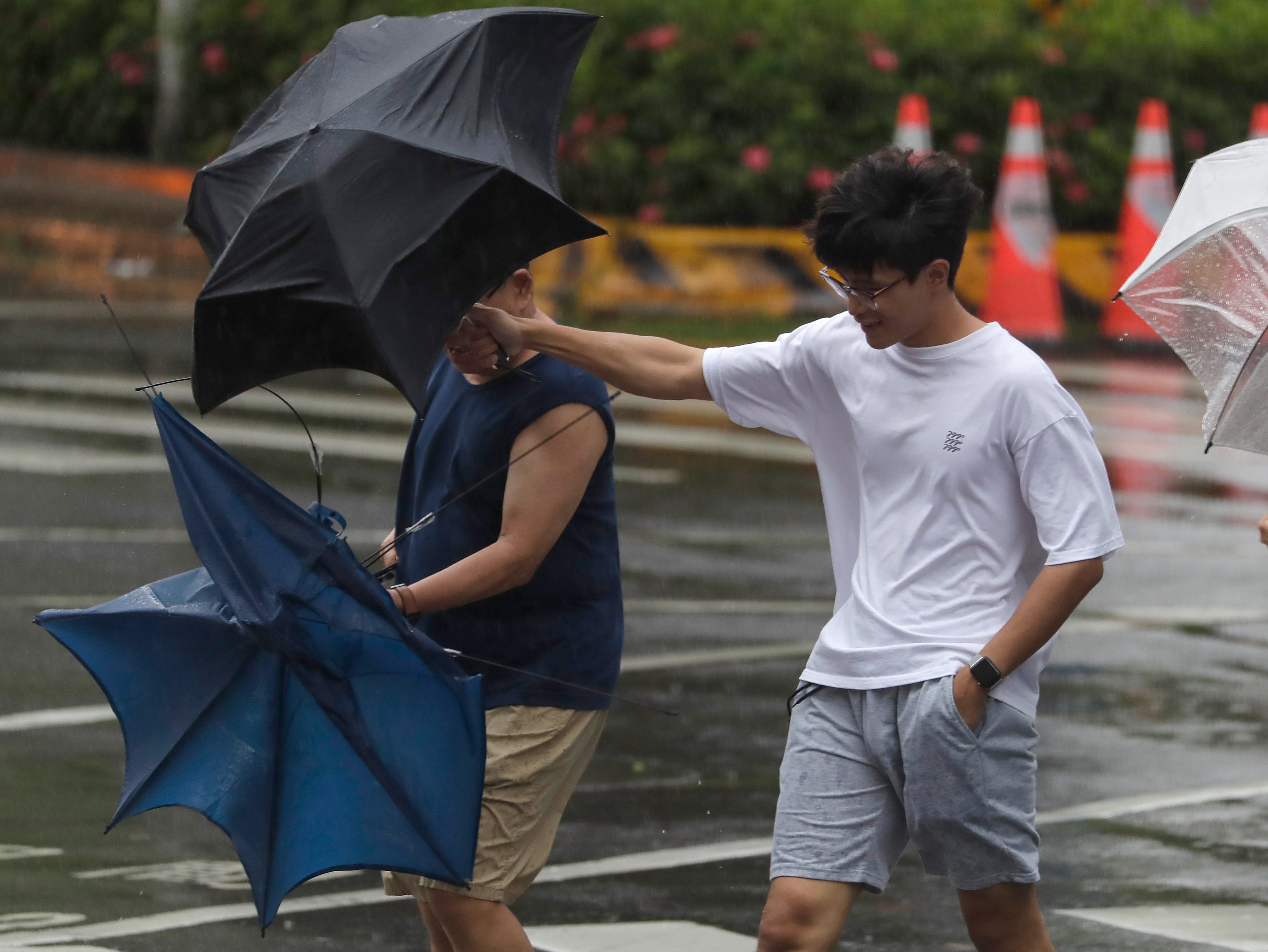 Two men struggle with their umbrellas against gusts of wind generated by Typhoon Gaemi in Taipei, Taiwan