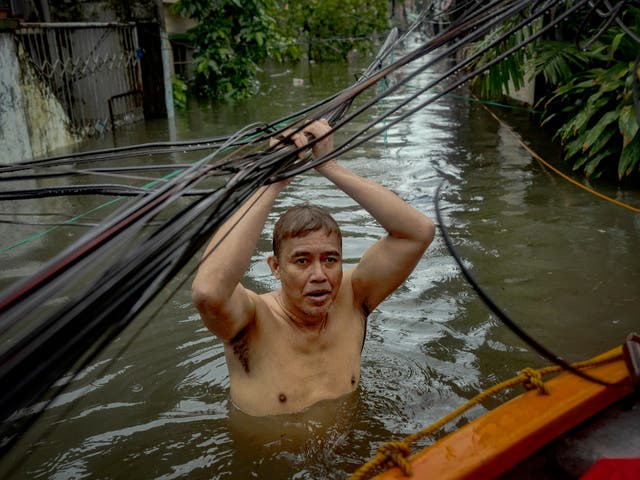 <p> A man holds on to power lines as he wades floodwaters in Quezon city, Philippines</p>