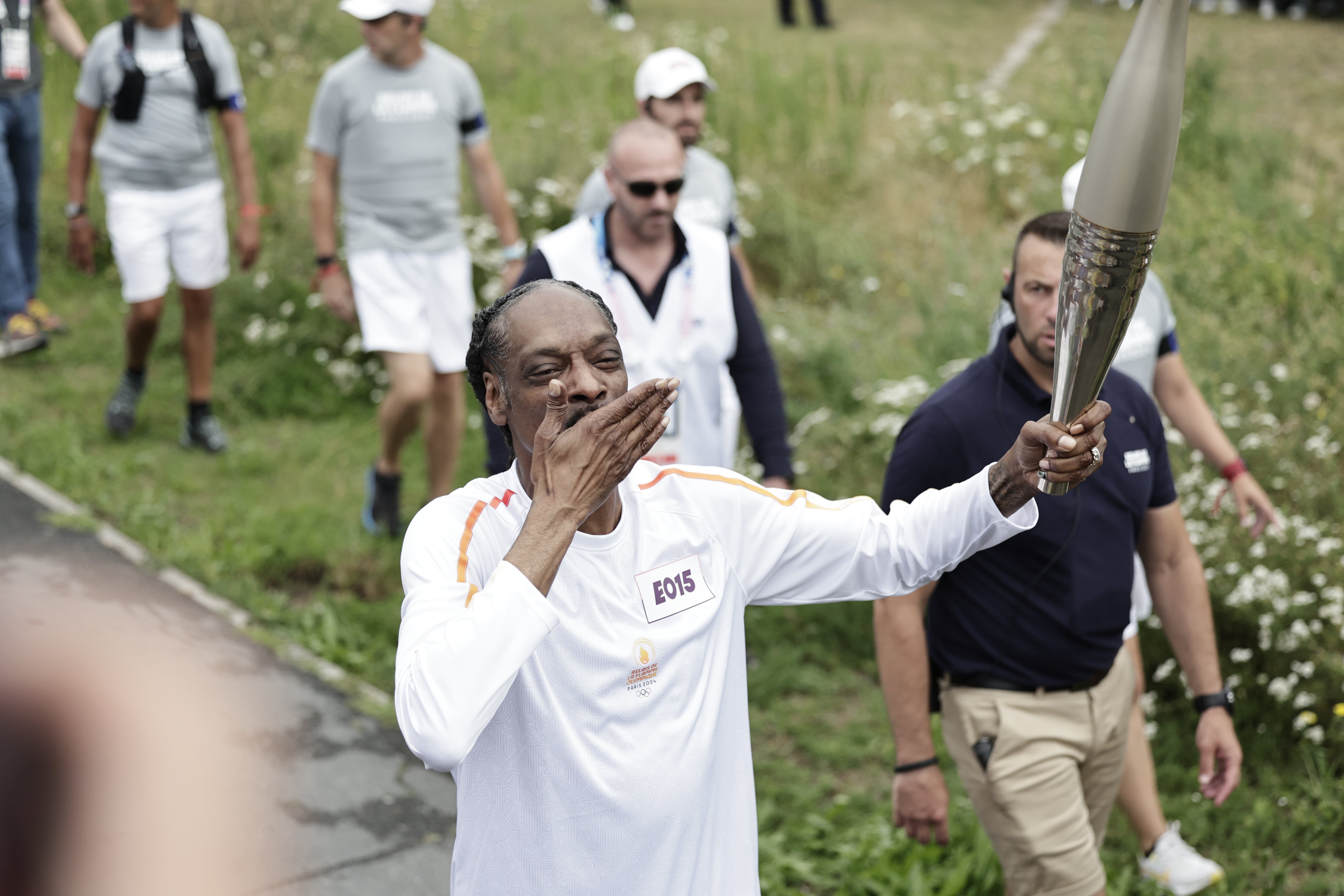 Snoop Dogg gestures as he holds the torch as part of the 2024 Paris Olympic Games Torch Relay