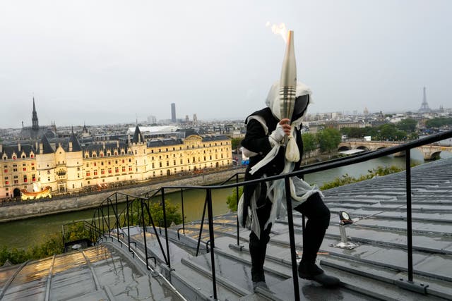 <p>Un portador de la antorcha lleva la llama olímpica sobre un edificio a lo largo del río Sena </p>