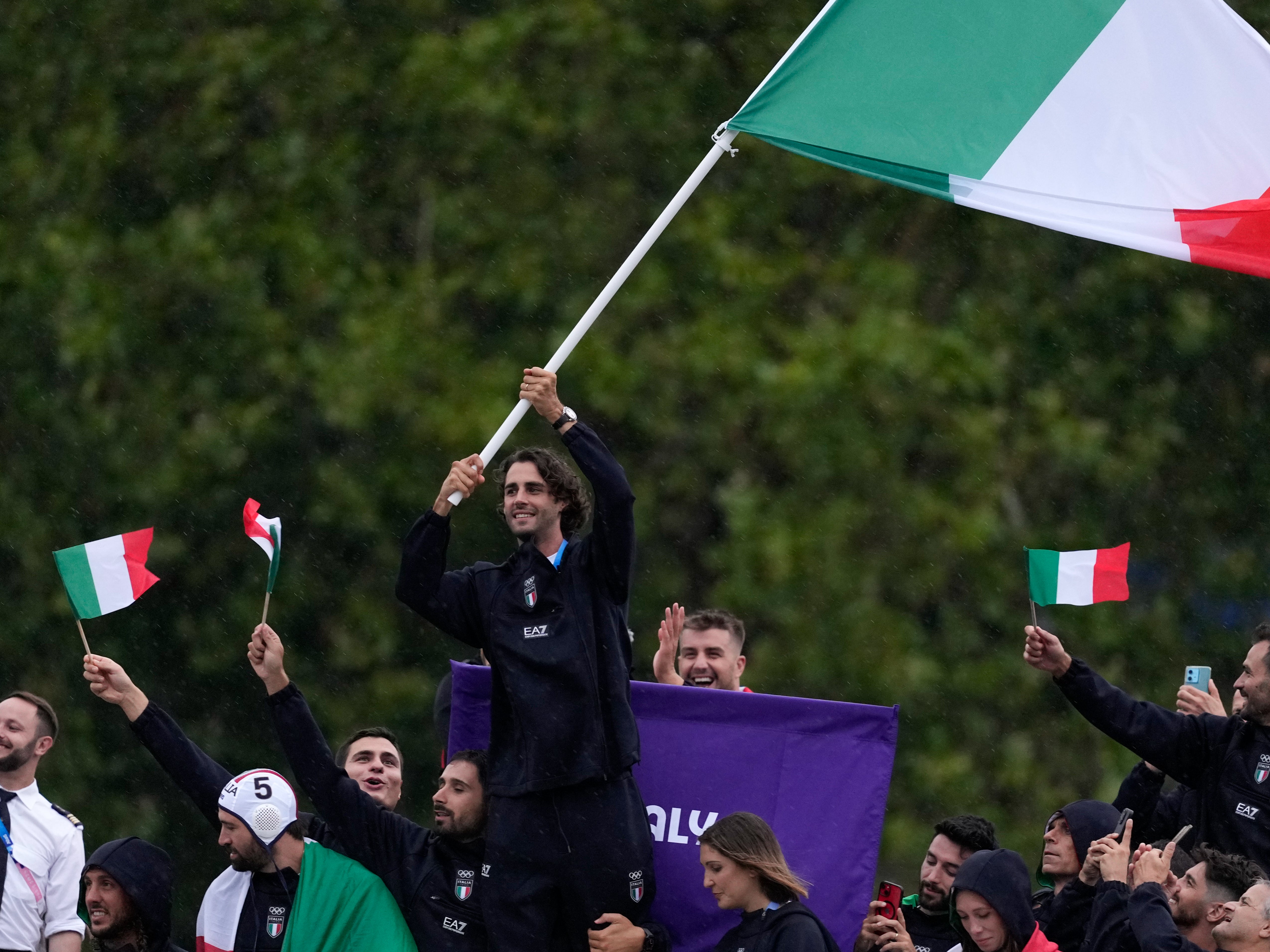 Gianmarco Tamberi waves an Italian flag as the Italian team parades along the Seine river in Paris