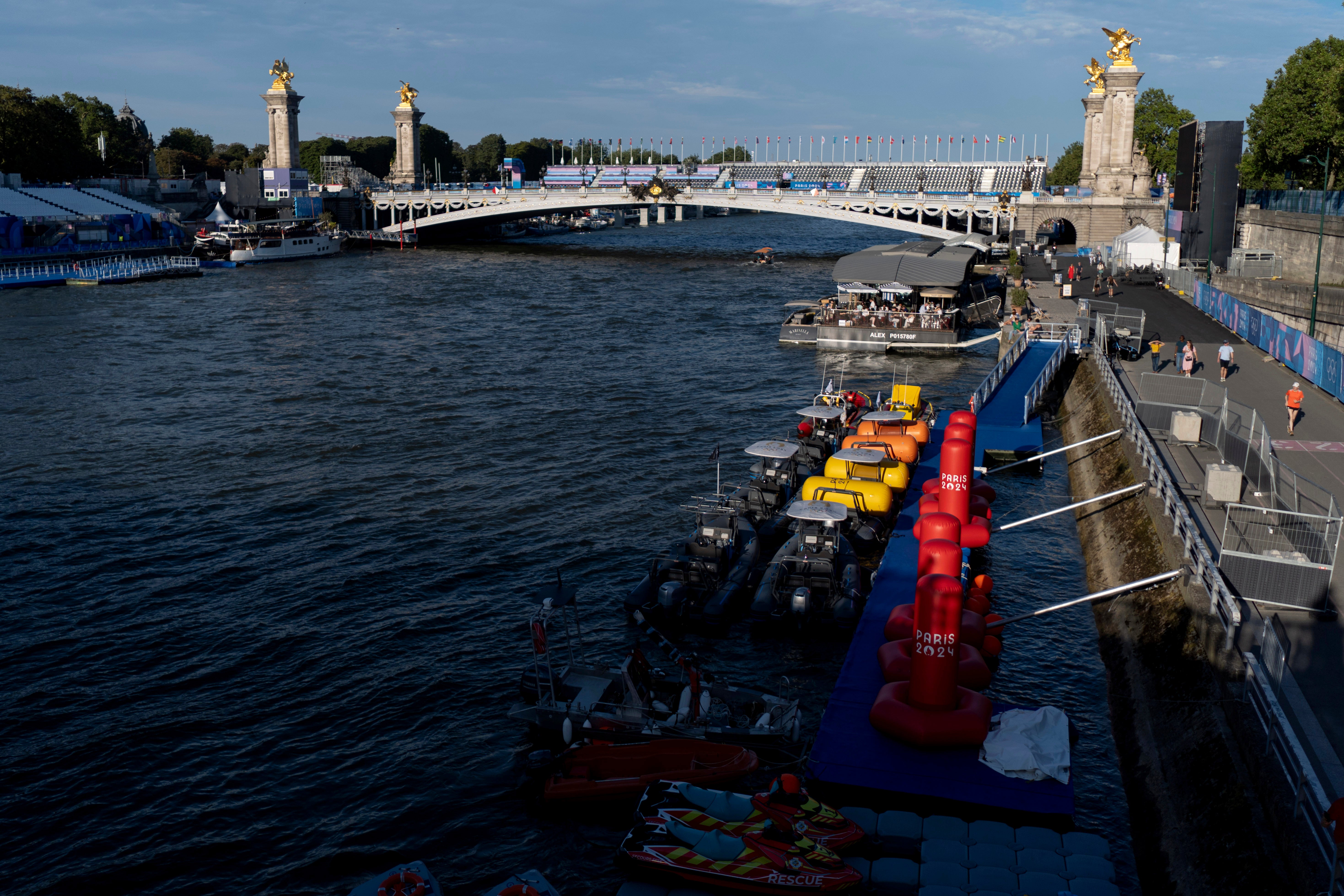 Watercraft and buoys sit along the Seine river as the triathlon event venue on the Pont Alexandre III bridge stands in the background