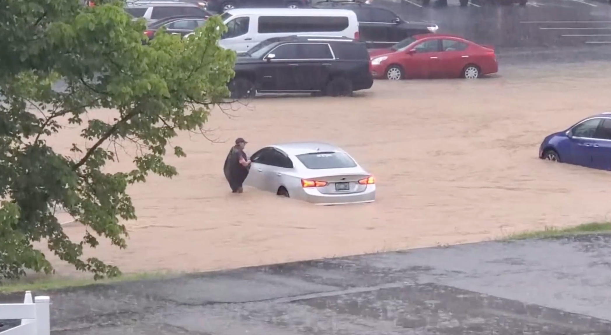 A person stands in waist-deep water next to a submerged car at Dollywood in Pigeon Forge, Tennessee as heavy rain causes flash flooding throughout the amusement park