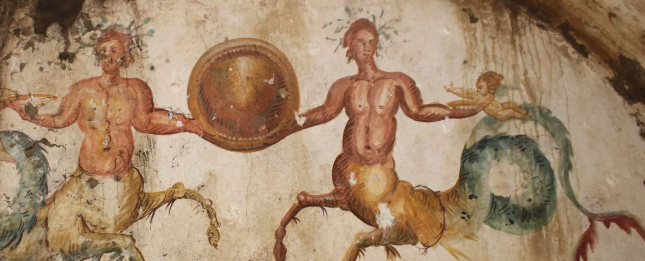 Tomb has a painting of two sea-centaurs holding a circular shield next to two babies