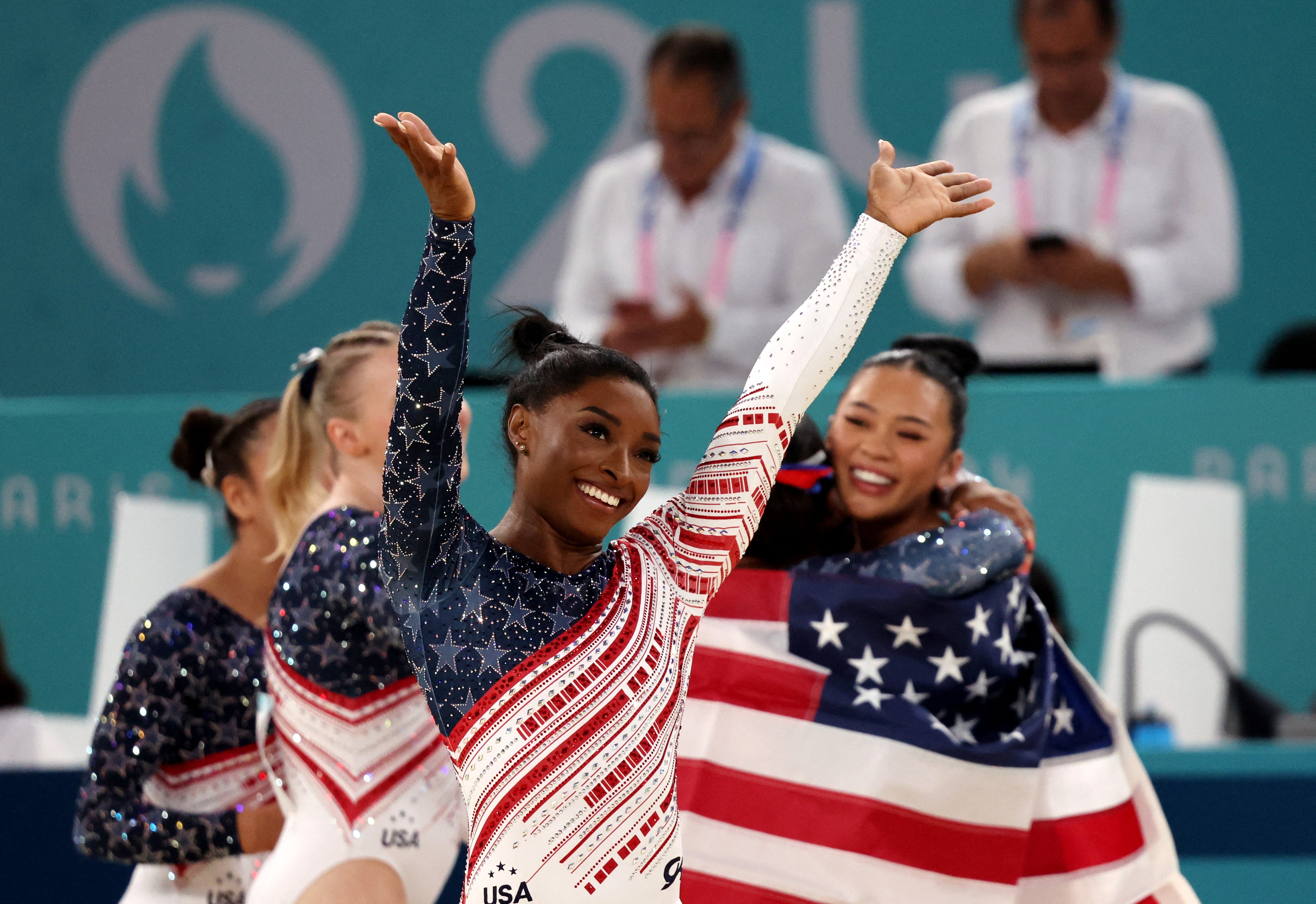 Simone Biles salutes the American fans as her teammates celebrate at the women’s team final