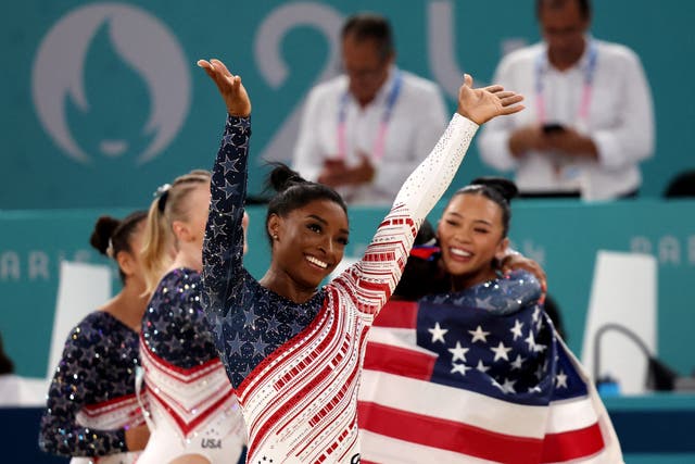 <p>Simone Biles saluda a la afición estadounidense mientras sus compañeras celebran</p>