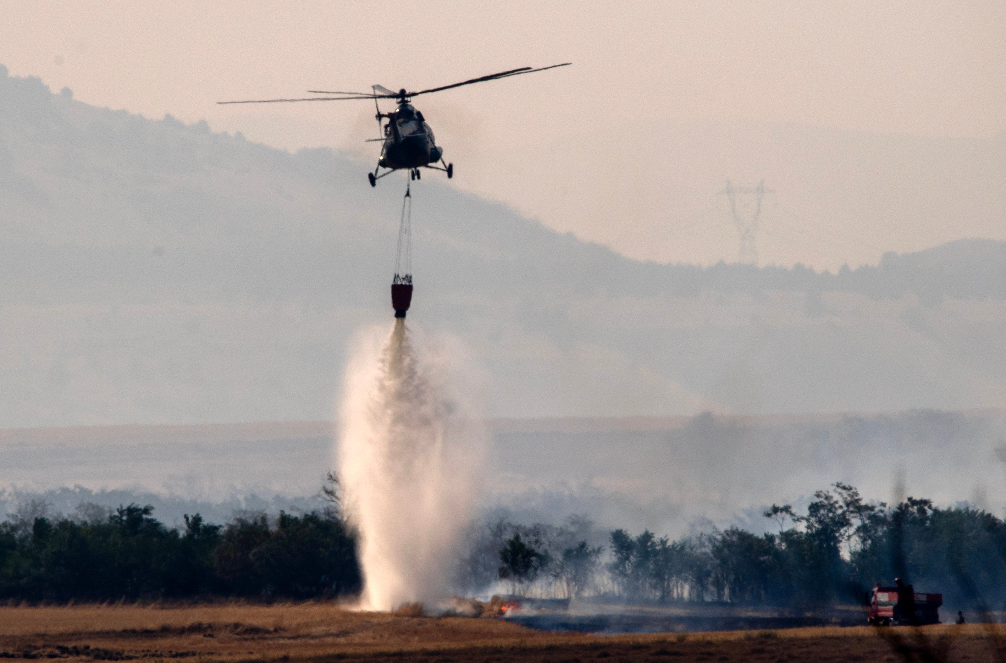 A firefighting helicopter drops water over the area affected with wildfires next to the village of Nemanjits, North Macedonia