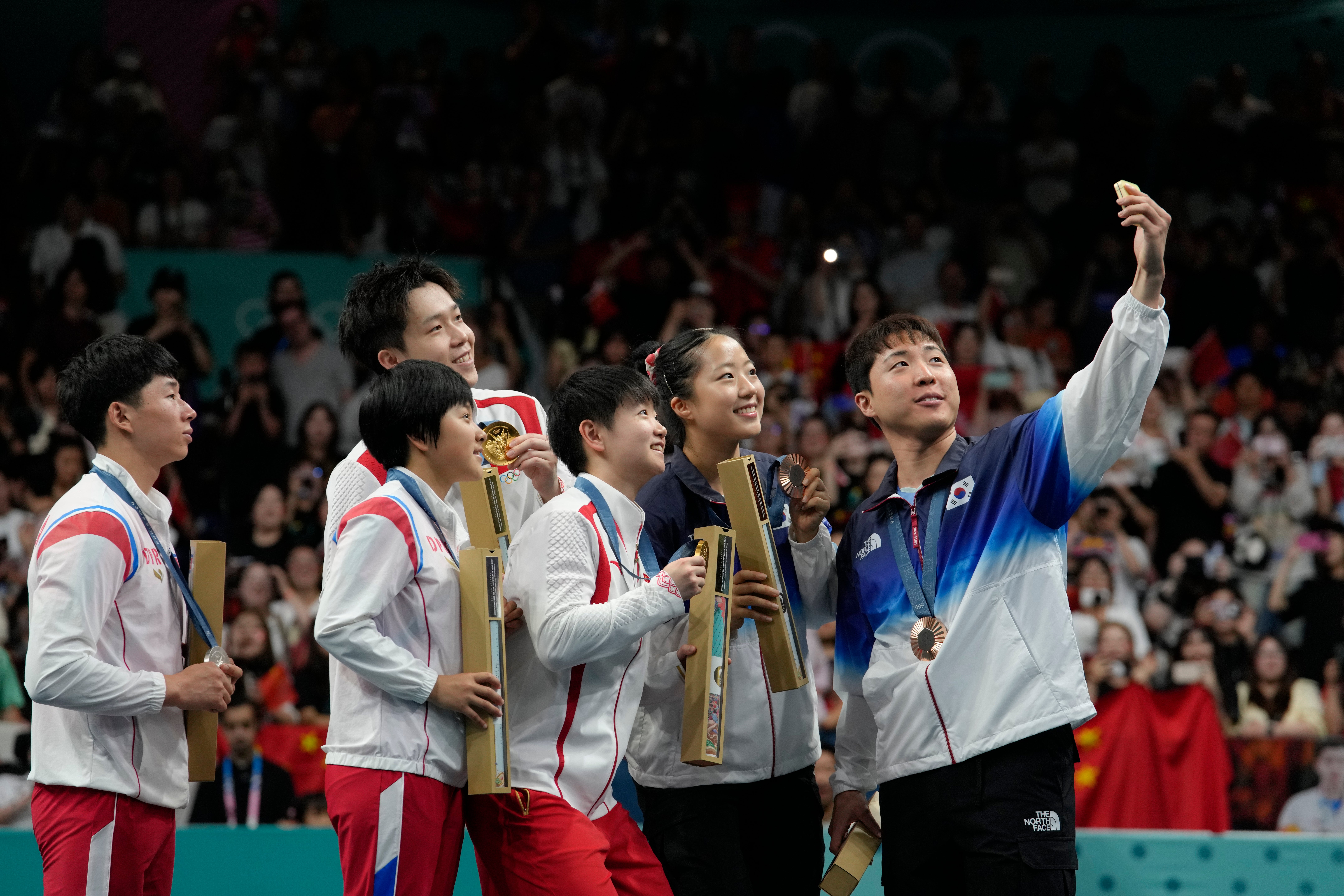 South Korea's Lim Jonghoon, right, takes a selfie with North Korea's Ri Jong-sik, left, and Kim Kum Yong, second left, China's Wang Chuqin, background, and Sun Yingsha, center, and his teammate Shin Yubin