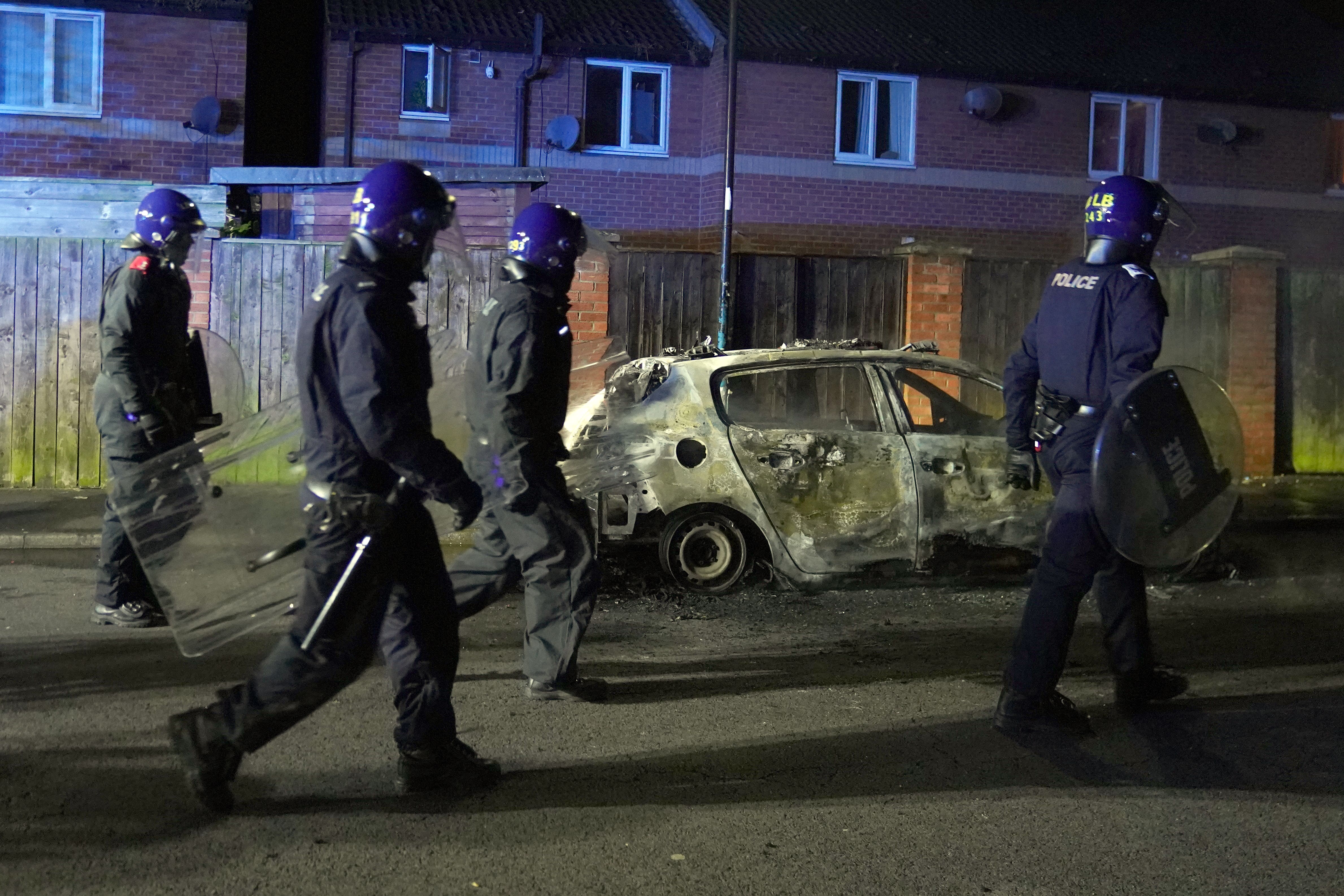 Officers walk past a burnt out police vehicle as they are deployed on the streets of Hartlepool (PA)