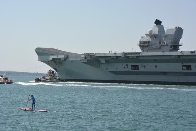 A stand-up paddle boarder accompanies the Royal Navy aircraft carrier HMS Prince of Wales out of Portsmouth Harbour (Ben Mitchell/PA)