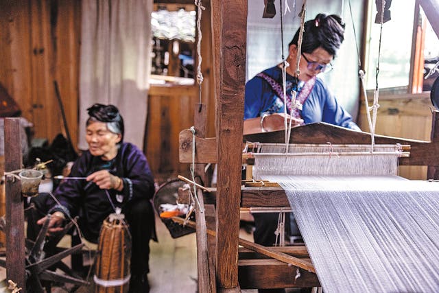 <p>Yang Shenghua weaves Dong cloth on a loom, with her mother Yang Xiuying spinning threads by her side at their home in Dali Dong village, Rongjiang county, Guizhou province</p>