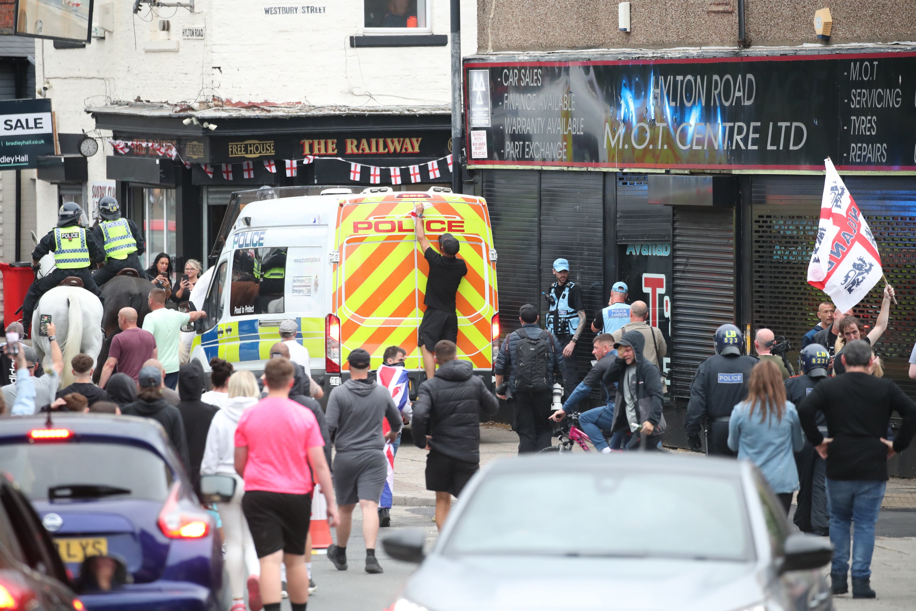 A man climbs on the back of a police van as people watch on