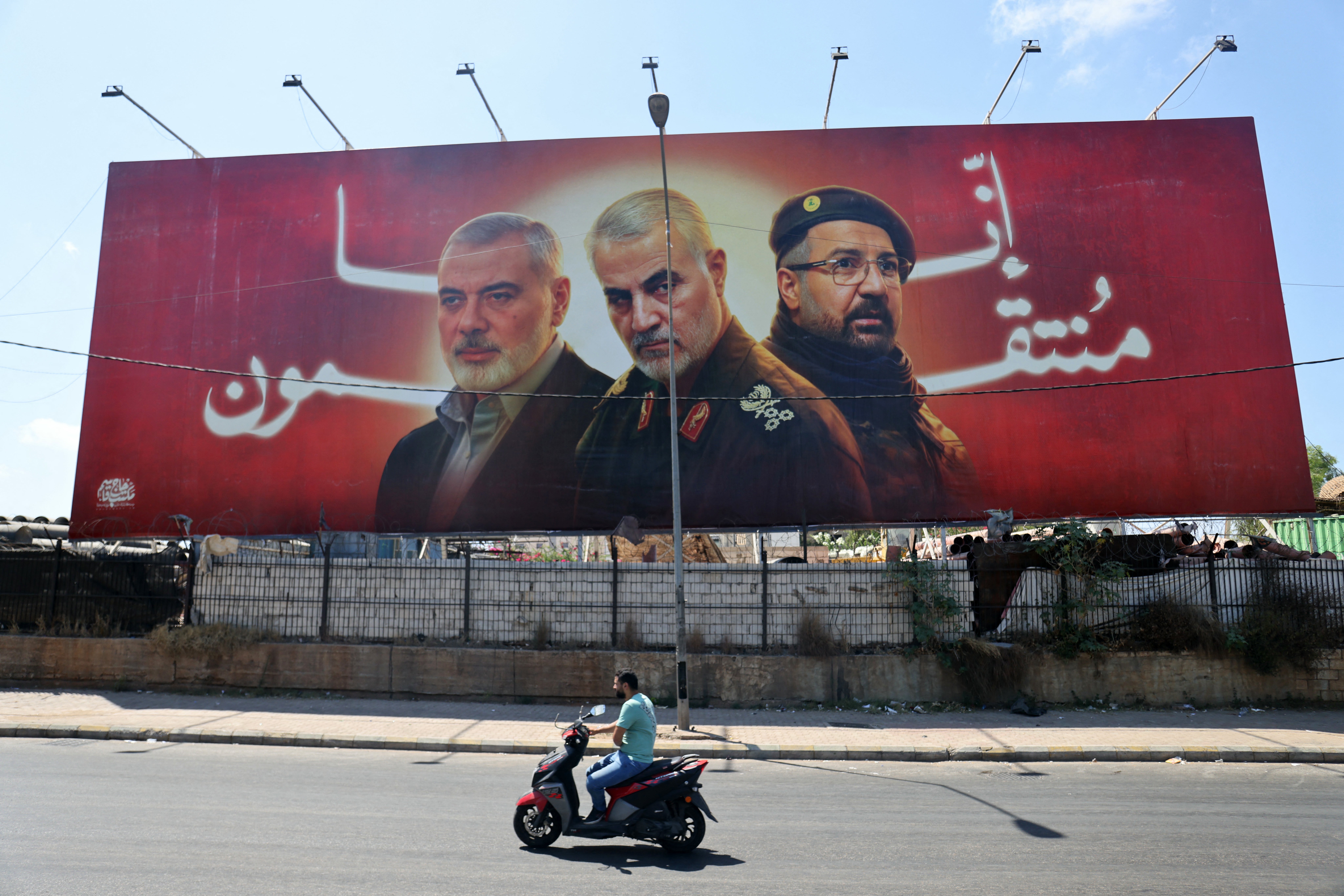 A man rides his moped past a billboard bearing portraits of slain leaders, Ismail Haniyeh of the Palestinian militant group Hamas, Iranian Quds Force chief Qasem Soleimani (C), and Hezbollah senior commander Fuad Shukr on the main road near the Beirut International Airport