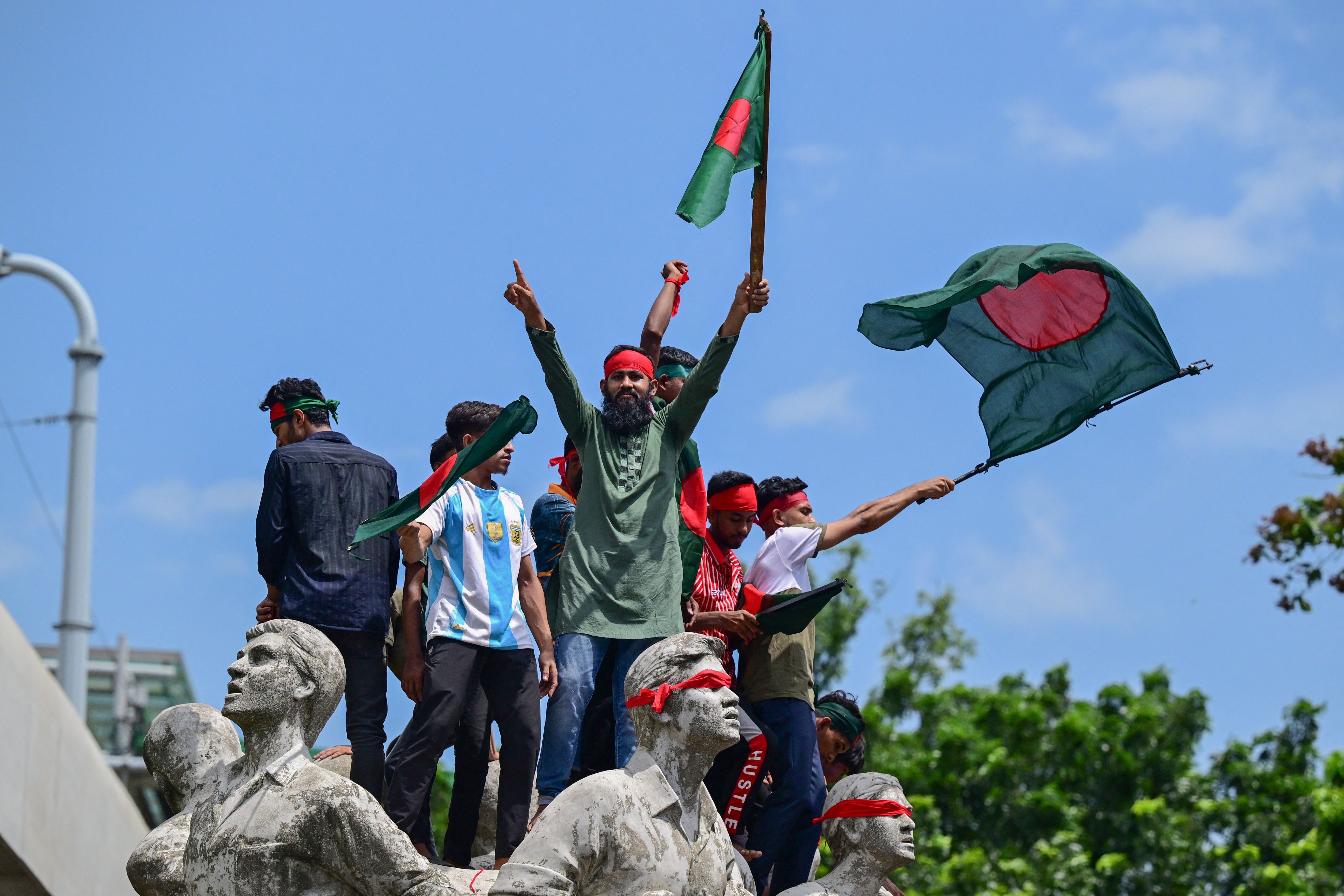 Protesters wave national flags as they stand over the Anti Terrorism Raju Memorial Sculpture in capital Dhaka, Bangladesh