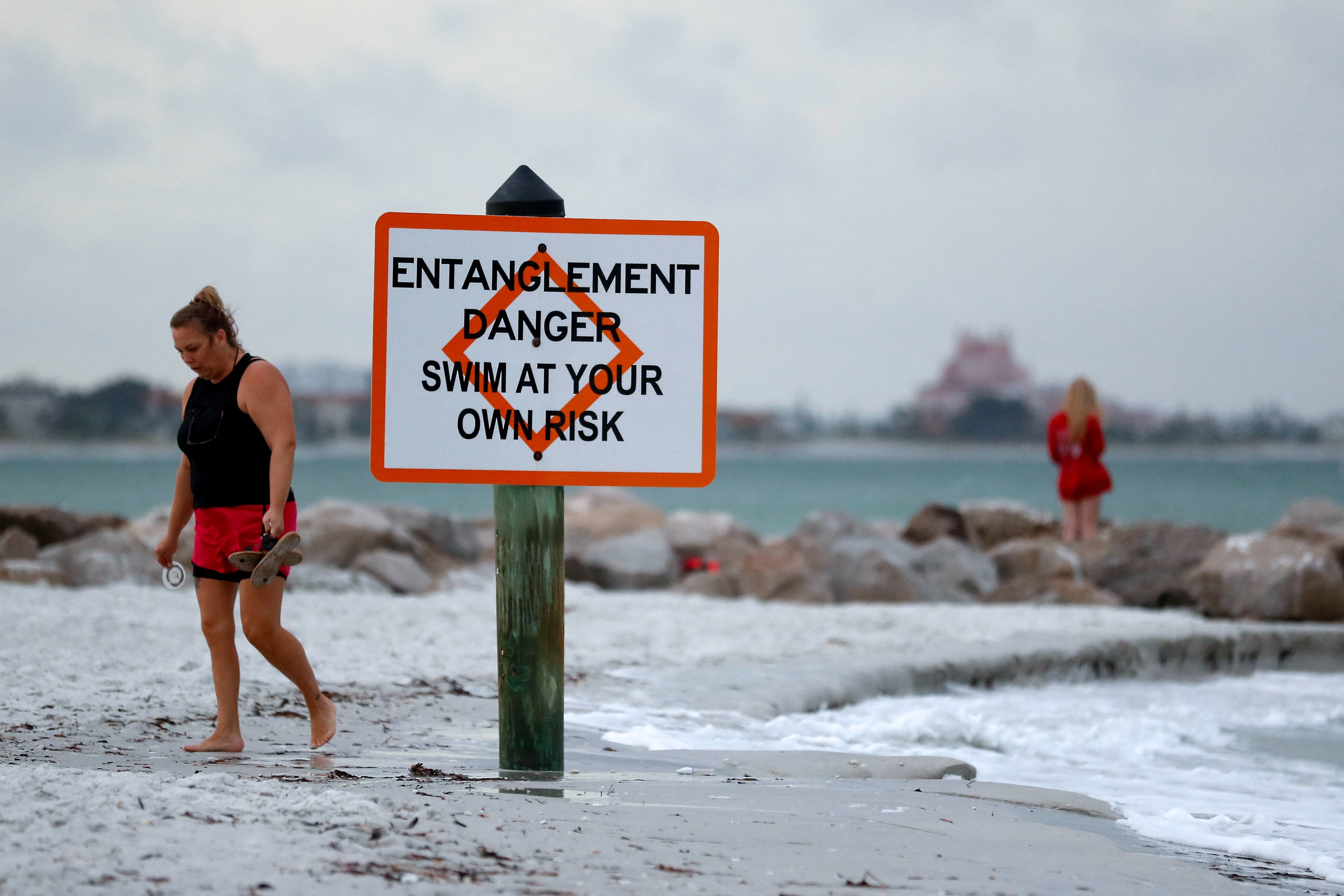 People walk along St. Pete Beach, Florida during cloudy weather on Sunday as Tropical Storm Debby approaches