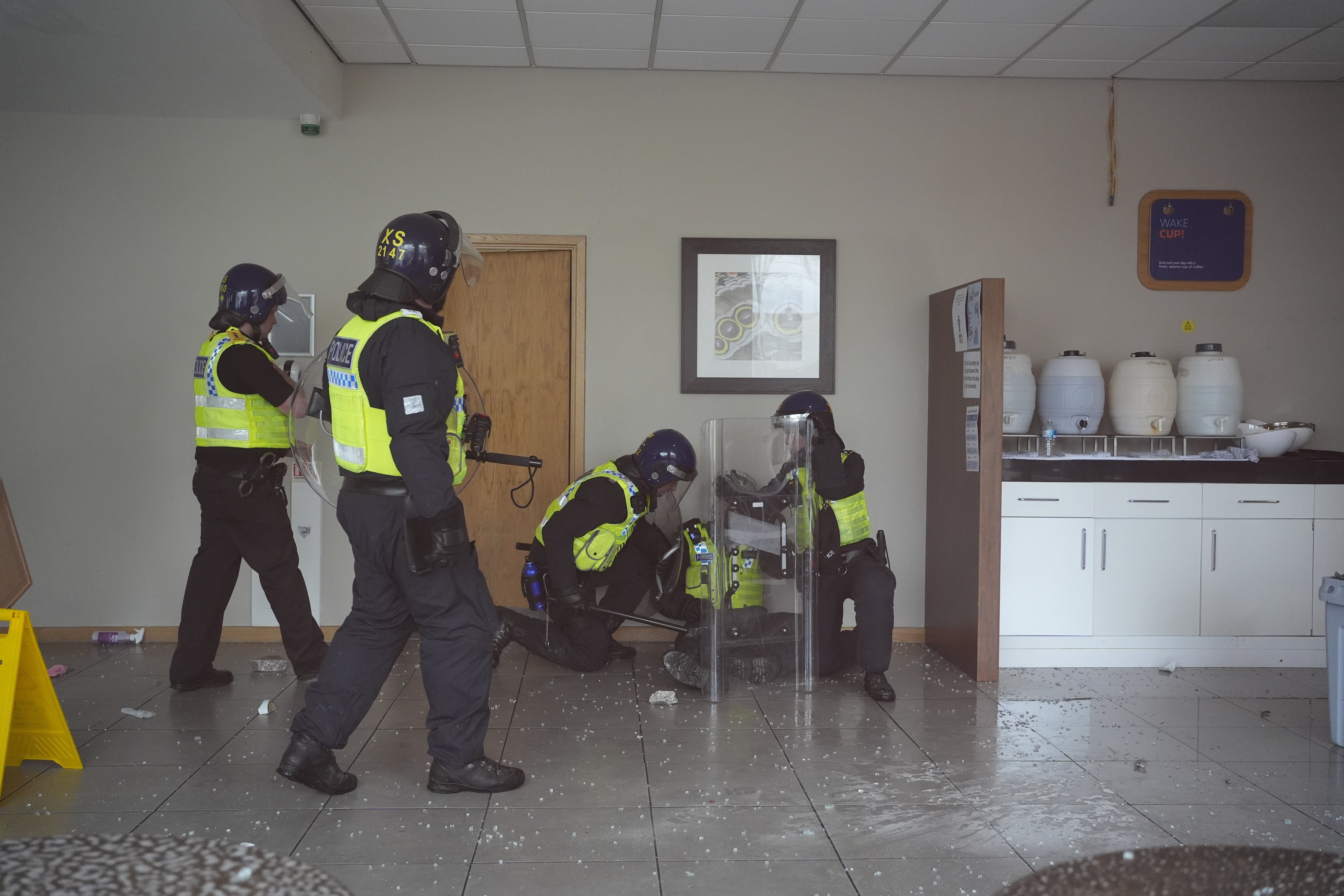 Police officers tend to a wounded colleague inside the hotel as seen through a smashed window