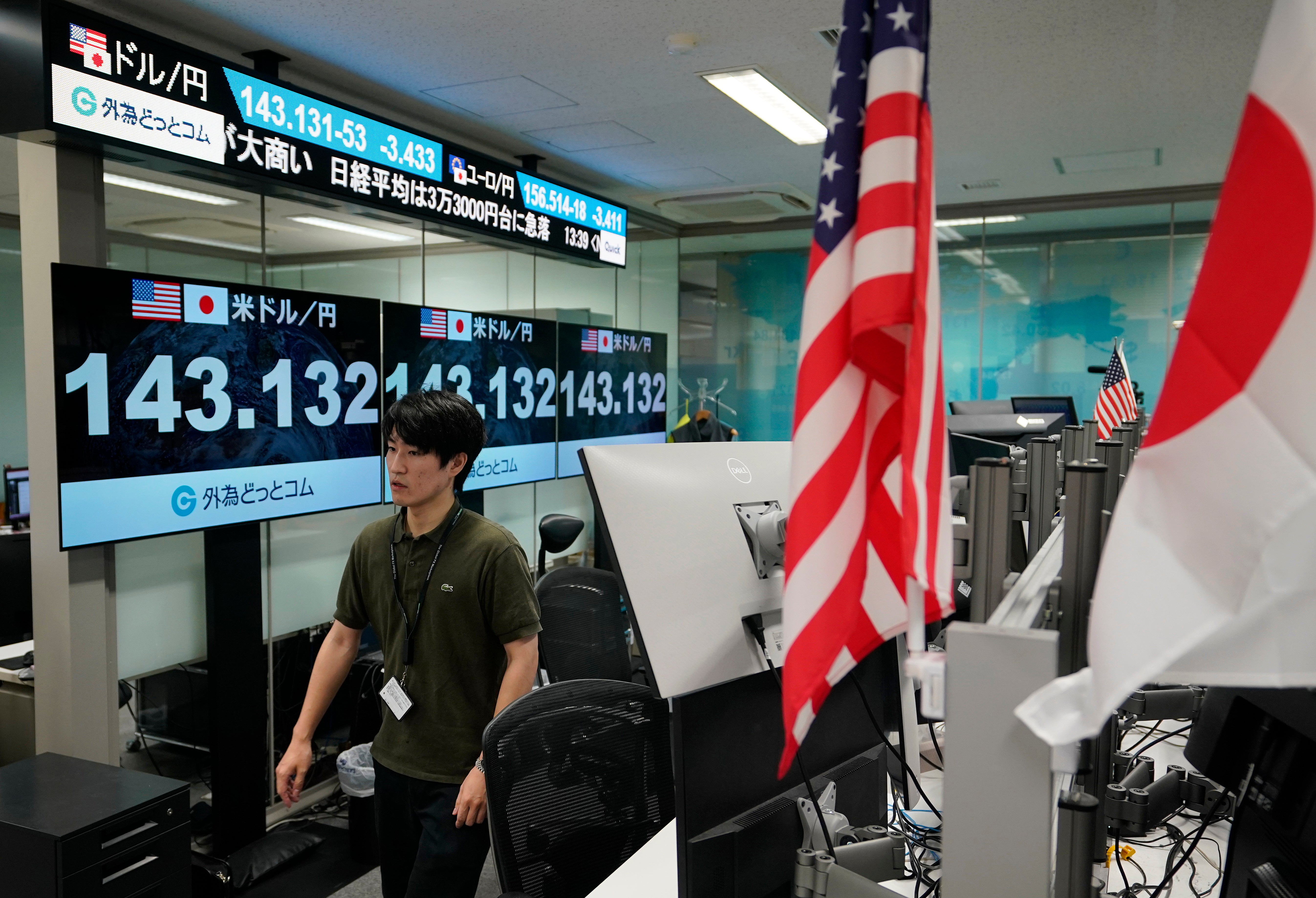 A dealer walks next to monitors showing foreign exchange rates in Tokyo, Japan, on 5 August 2024