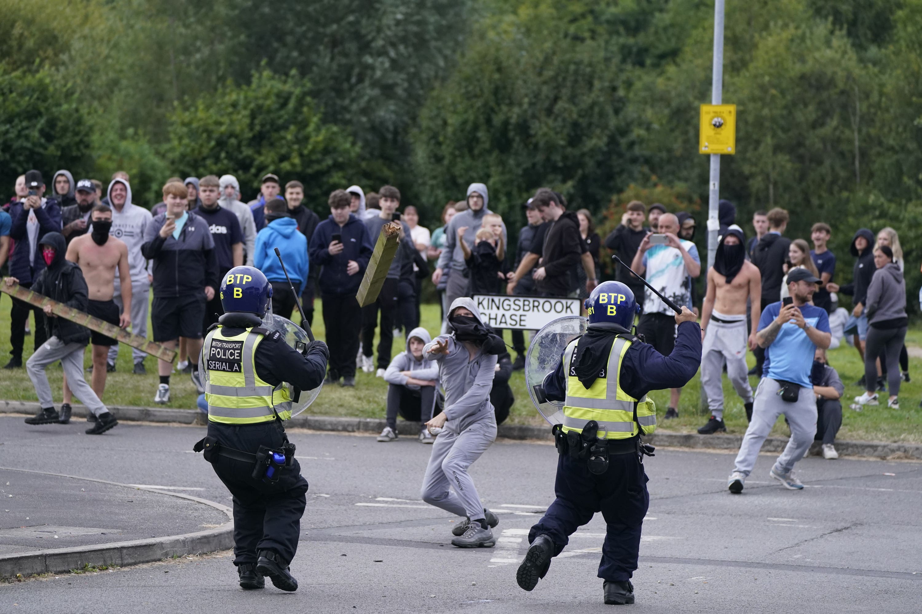 A youth wearing a grey tracksuit and with his face covered by a black T-shirt throws a fence post towards police in Rotherham (Danny Lawson/PA)