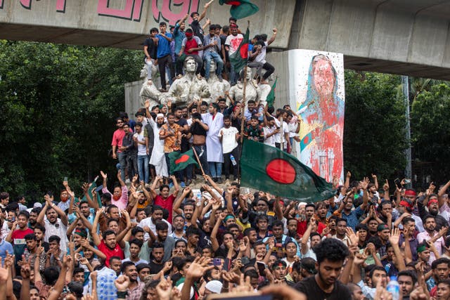 <p>Protesters climb a public monument as they celebrate after getting the news of Prime Minister Sheikh Hasina's resignation, in Dhaka</p>