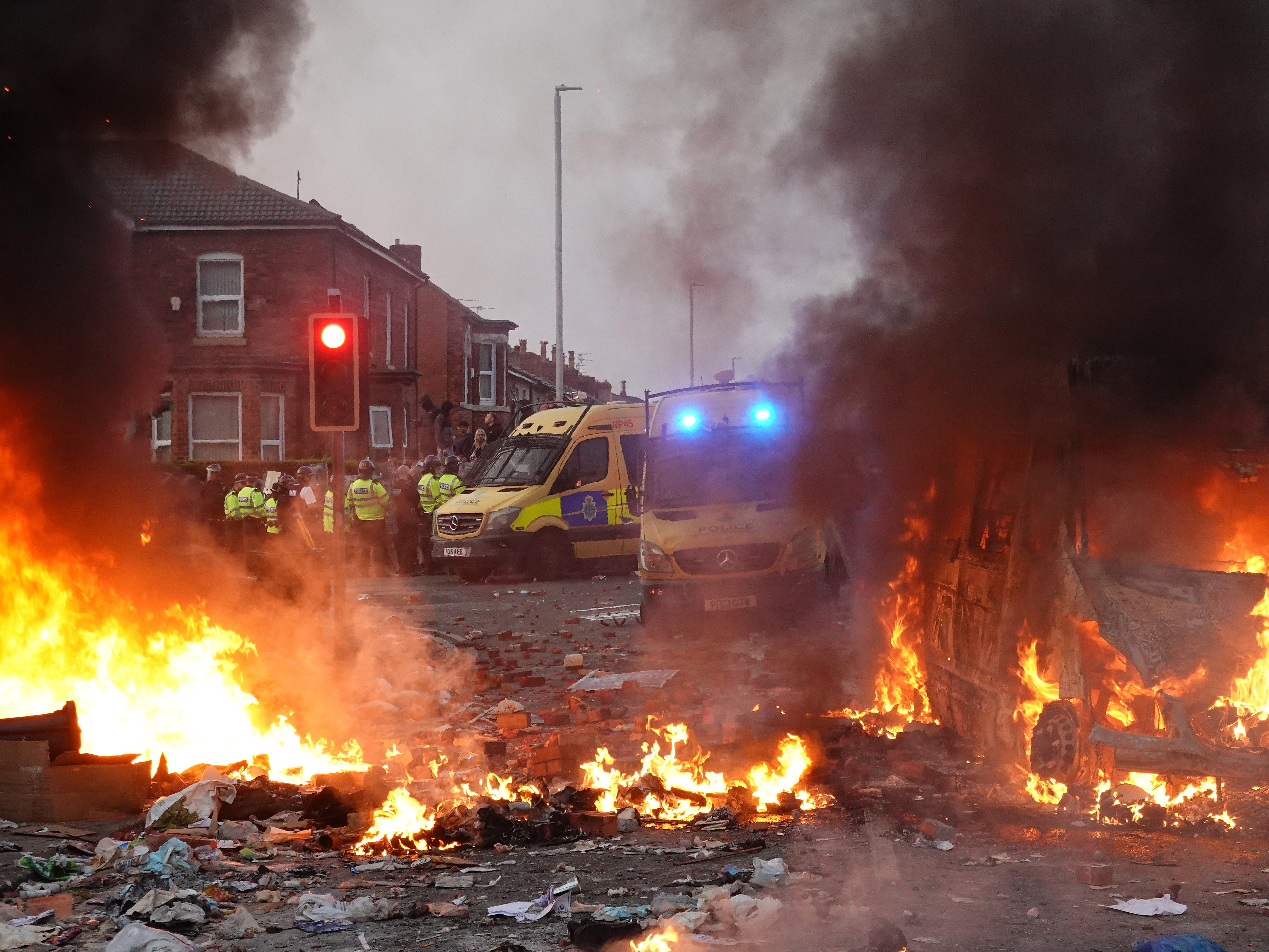 Riot police hold back protesters near a burning police vehicle after disorder broke out on 30 July in Southport