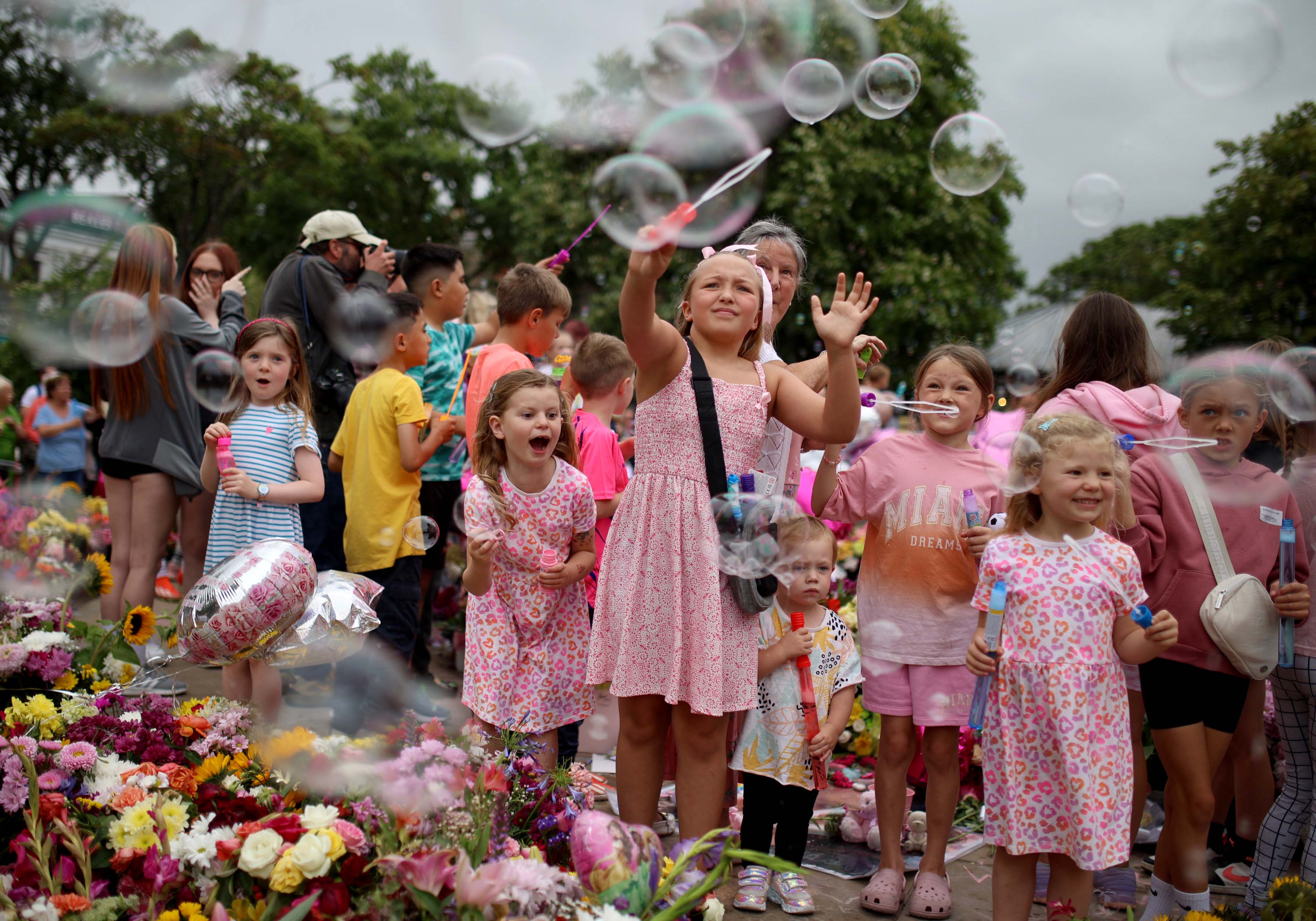 Young children play with bubble wands amongst floral tribute left outside the Town Hall in Southport, ahead of a vigil on Monday evening