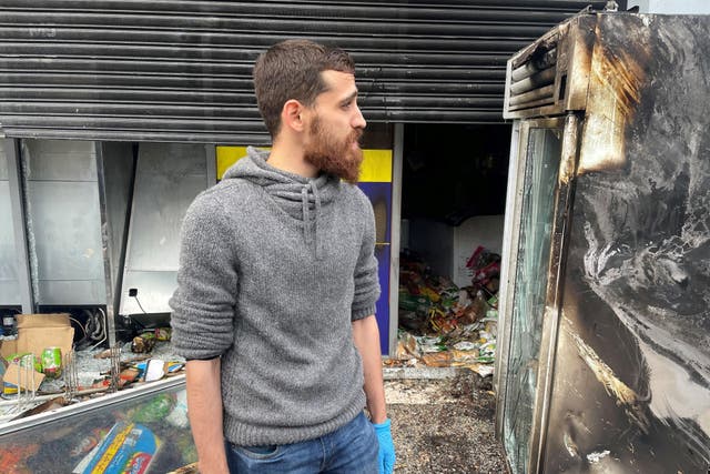 Manager Bashir (no surname given) outside his supermarket which was badly damaged by fire (Jonathan McCambridge/PA)